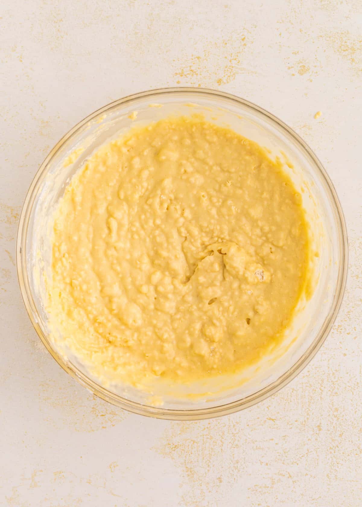A glass bowl filled with thick, yellow gluten-free coffee cake batter on a light surface.