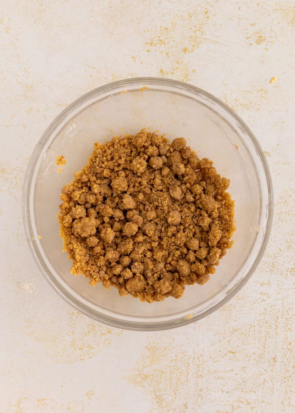 A glass bowl filled with gluten-free coffee cake mixture on a light surface.