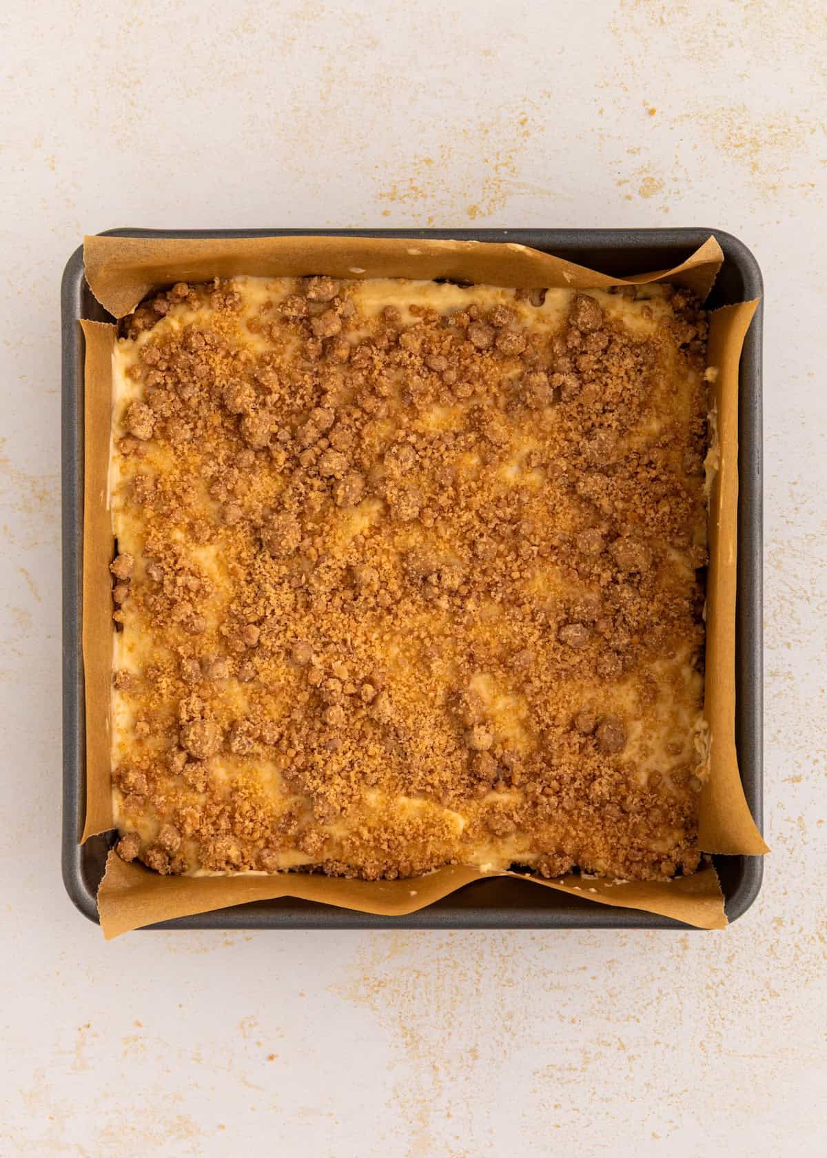 Gluten-free coffee cake with a golden brown crumb topping in a parchment-lined baking pan.