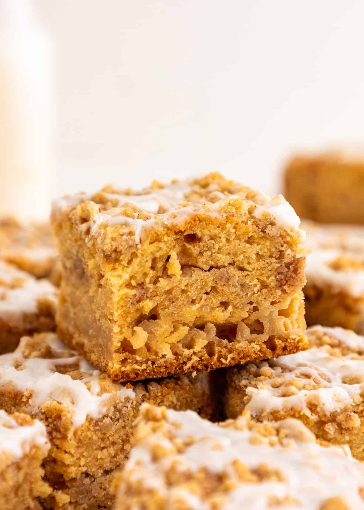 A close-up of a glazed gluten-free coffee cake square stacked on other cake pieces.