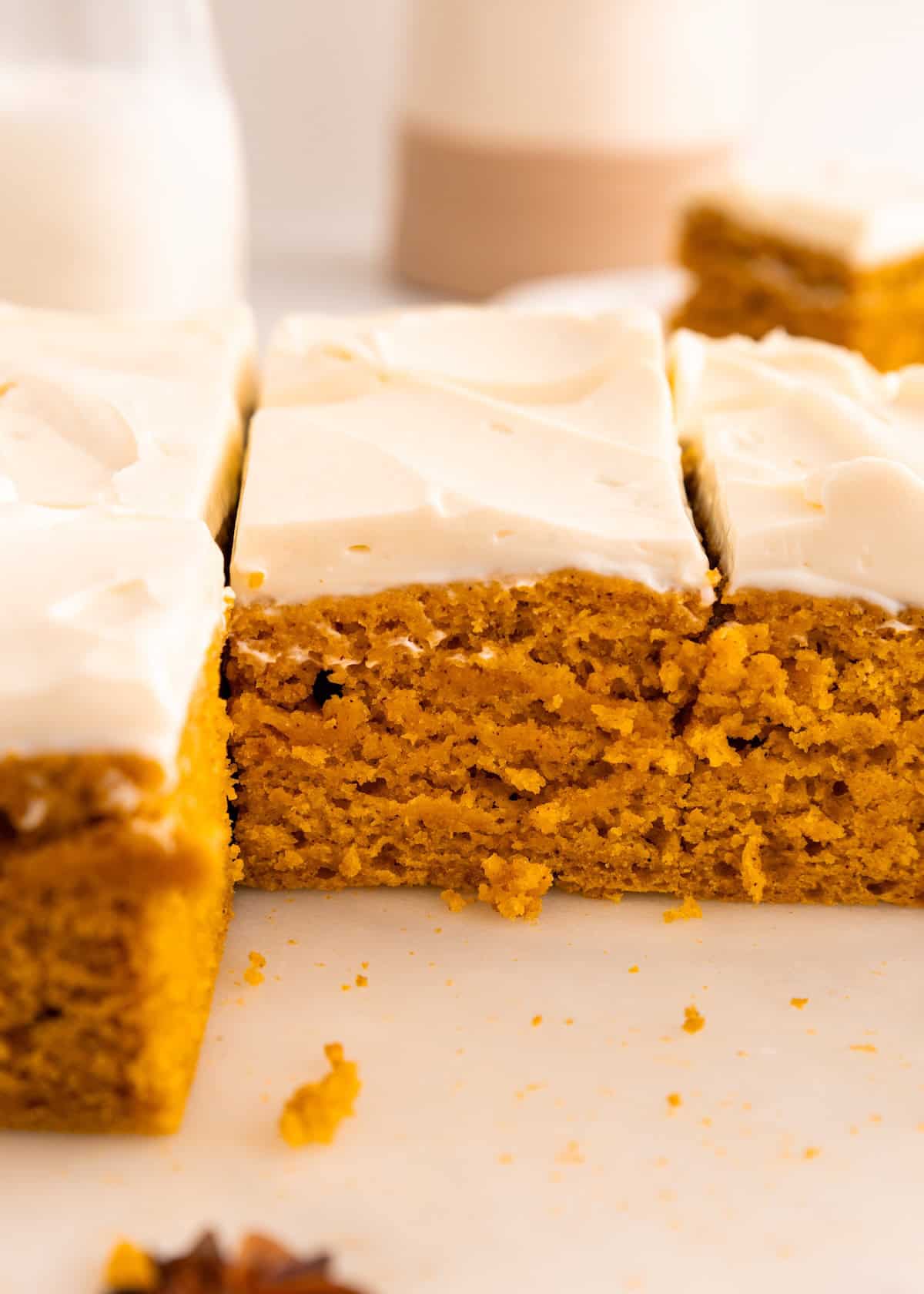 Gluten-free pumpkin cake with cream cheese frosting, sliced into squares on a white surface.