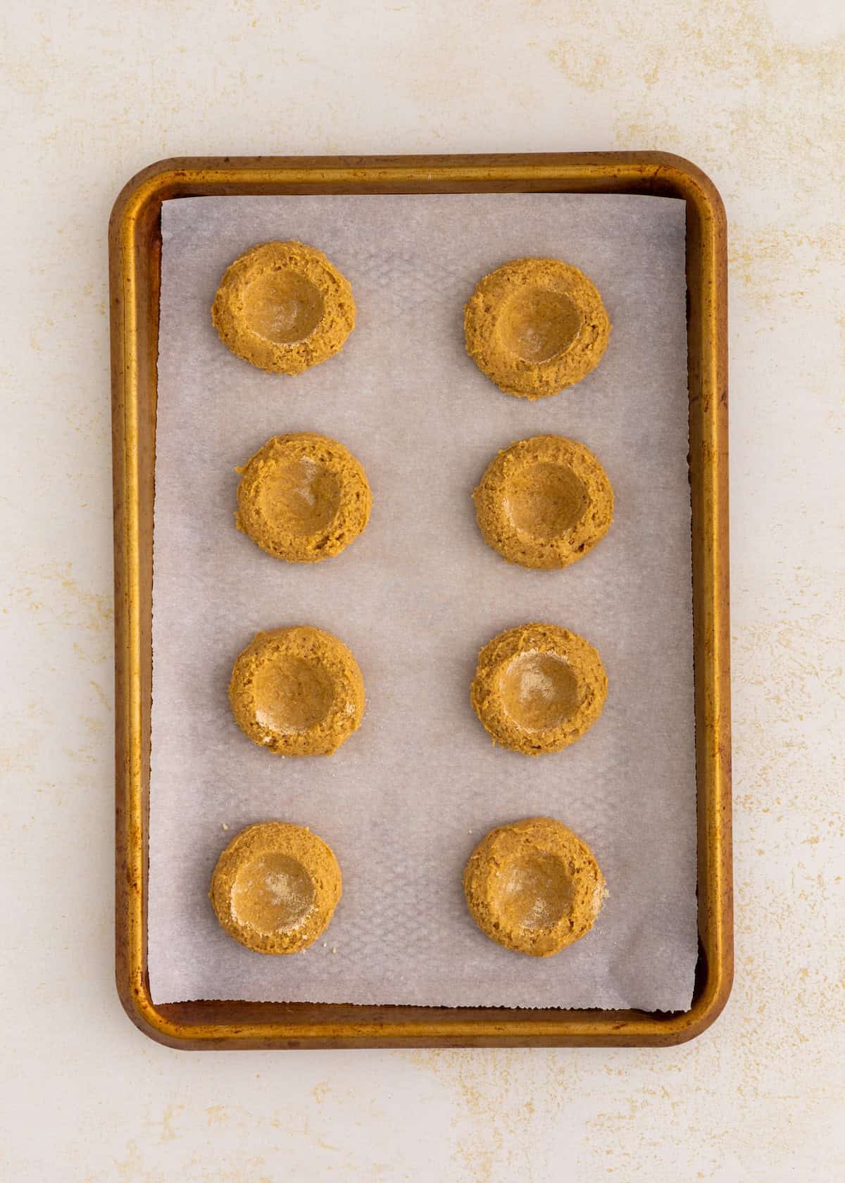 A baking sheet with eight gluten-free thumbprint cookies on parchment paper, ready to bake.