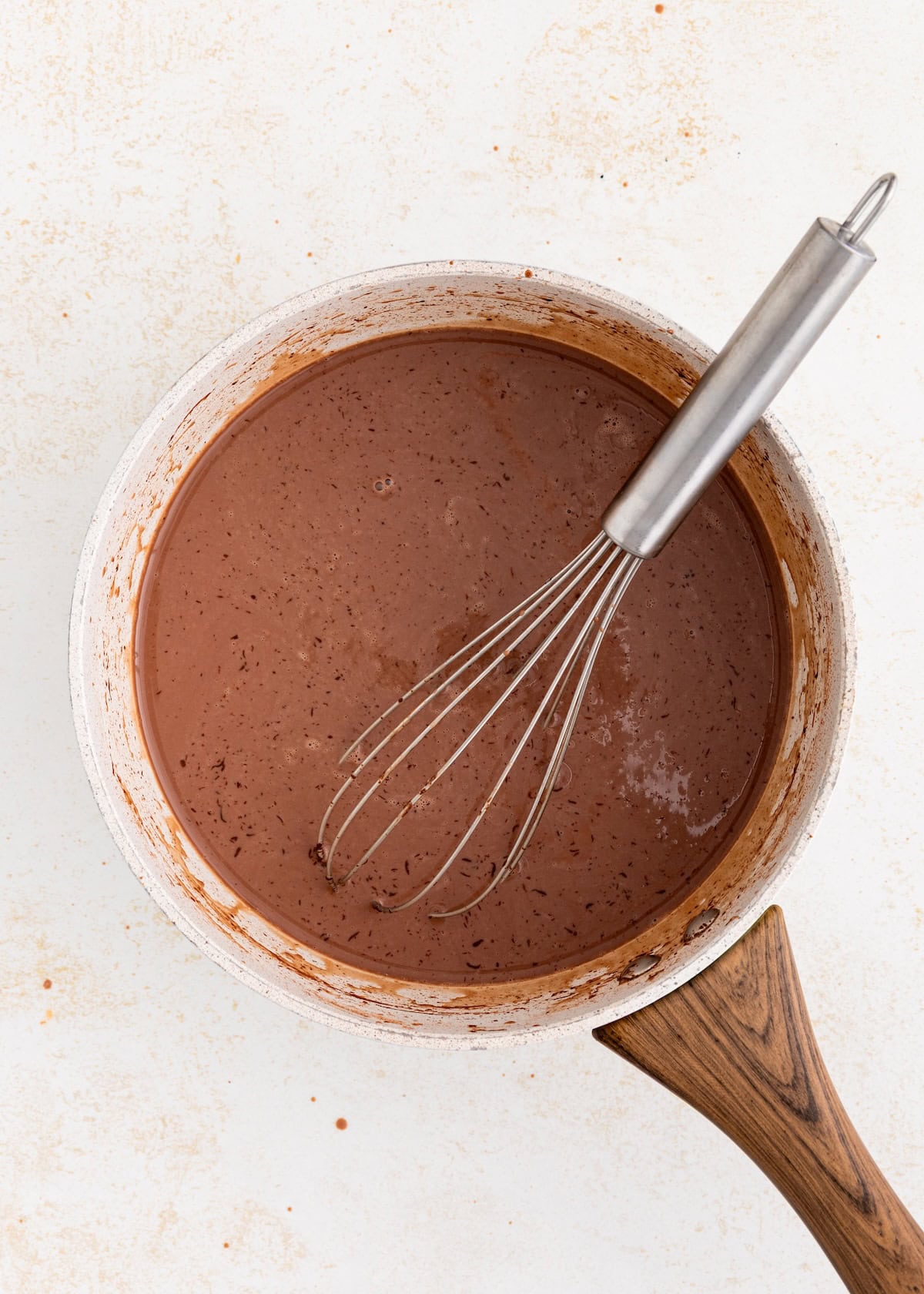 A saucepan of homemade fudgesicles mixture with a whisk on a light surface.