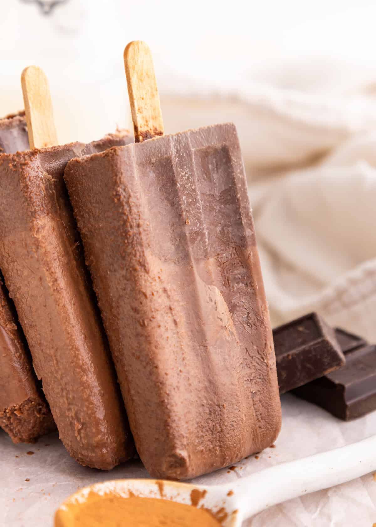 Two homemade fudgesicles on sticks with chocolate pieces in the background.