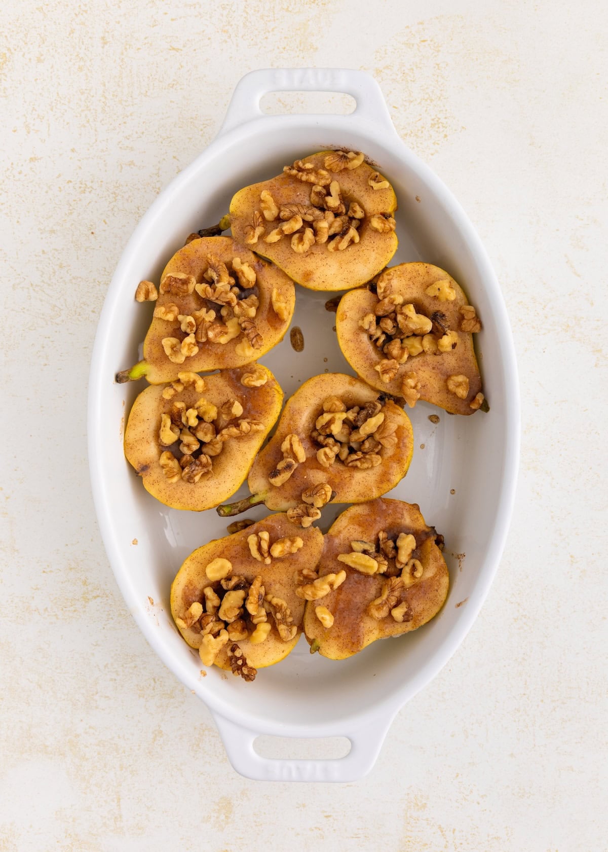 Honey baked pears topped with walnuts and cinnamon in a white oval baking dish.
