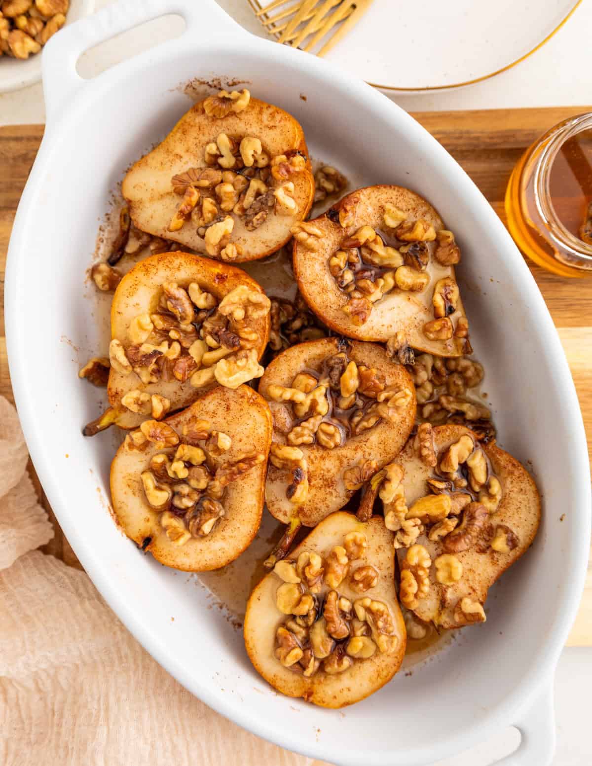 Honey baked pears topped with walnuts and spices in a white baking dish.