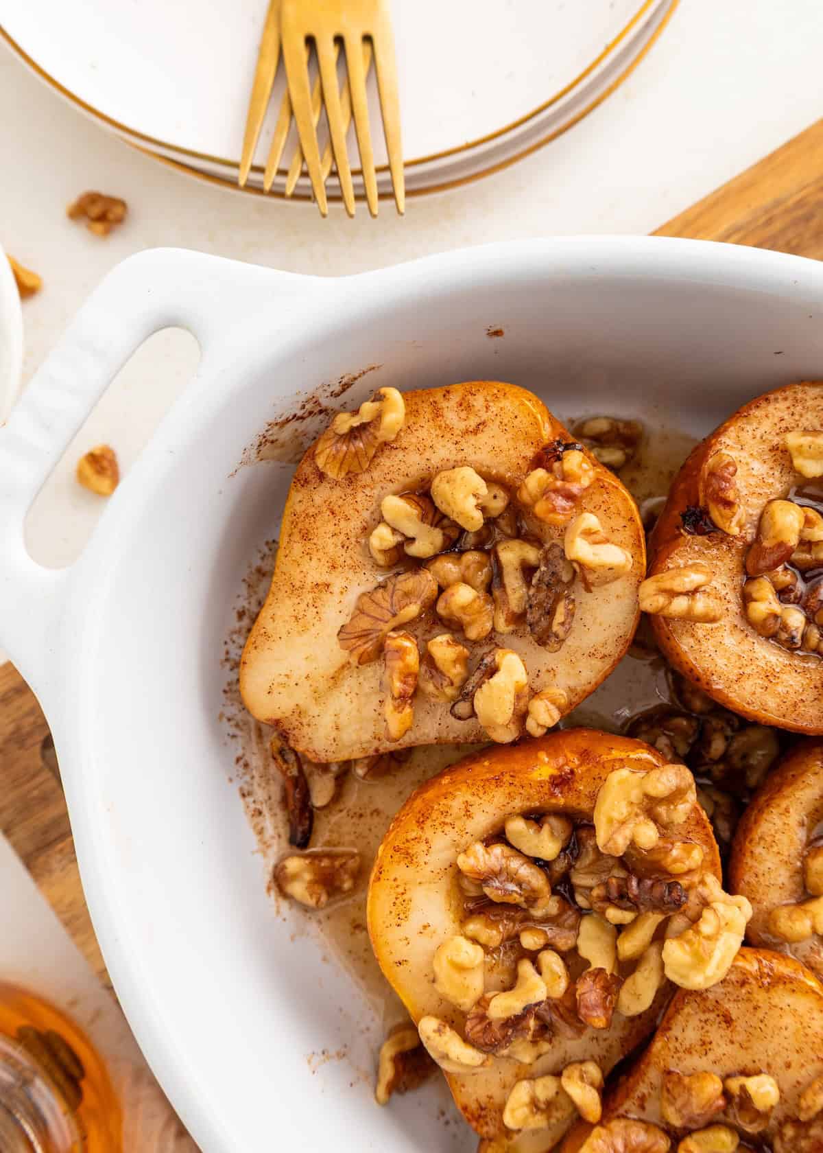Honey baked pears topped with walnuts in a white baking dish, with plates and forks nearby.