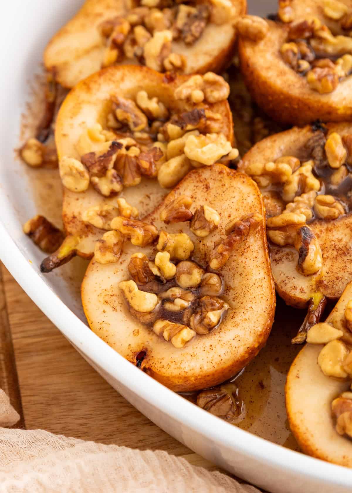 Honey baked pears topped with walnuts and cinnamon in a white dish.