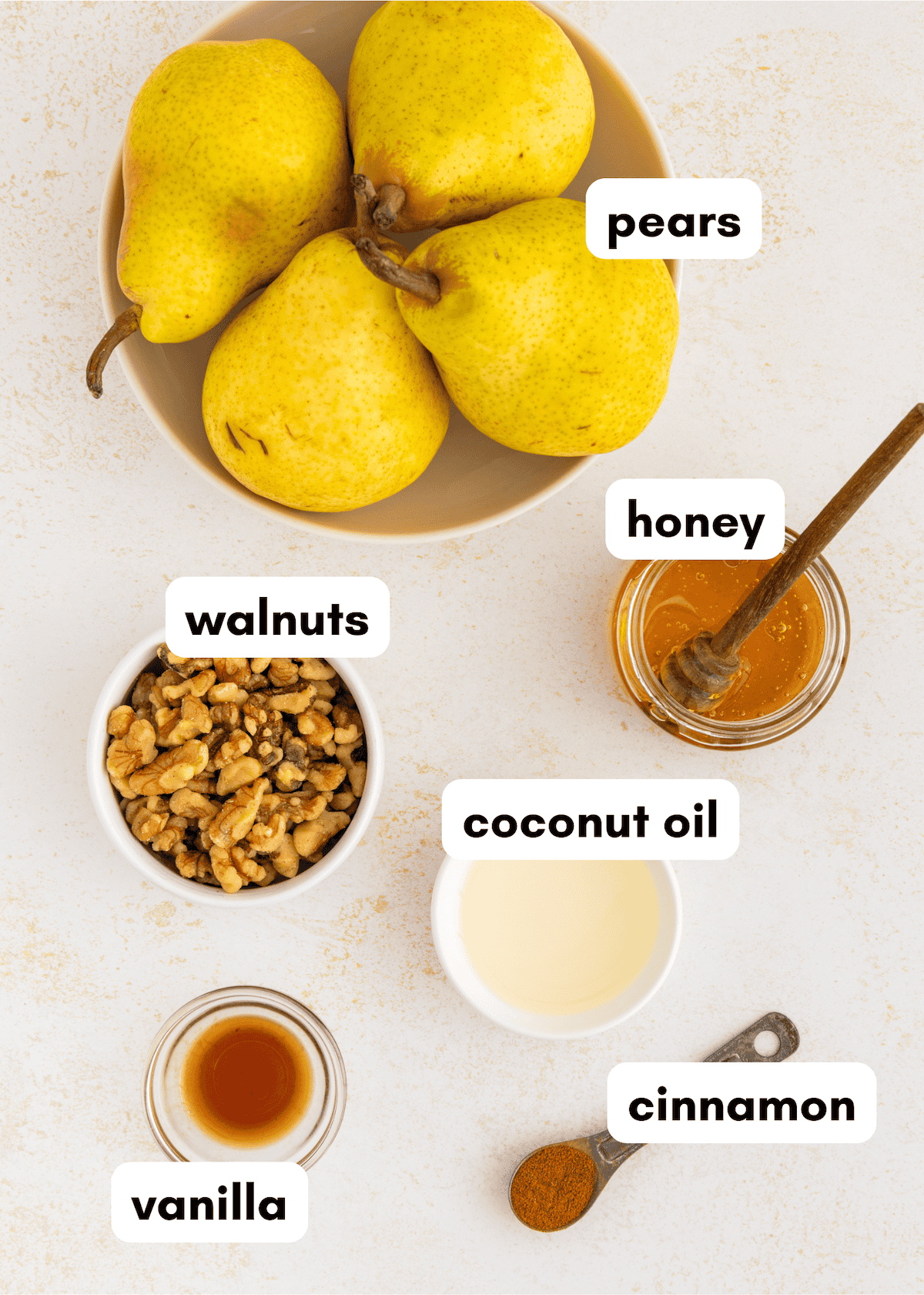 Bowl of honey baked pears, walnuts, coconut oil, cinnamon, and vanilla on a white surface.