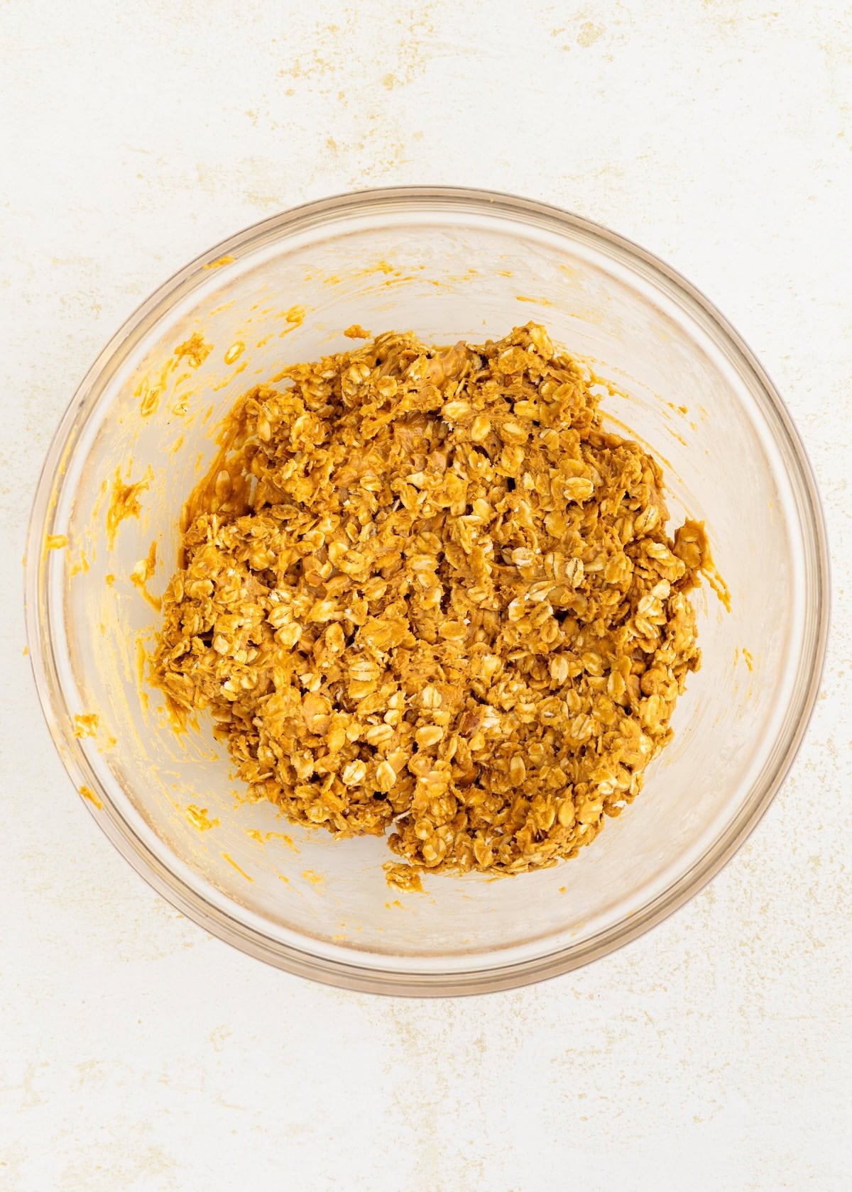 A glass bowl filled with an oat and pumpkin mixture for Peanut Butter Oat Cups on a light surface.