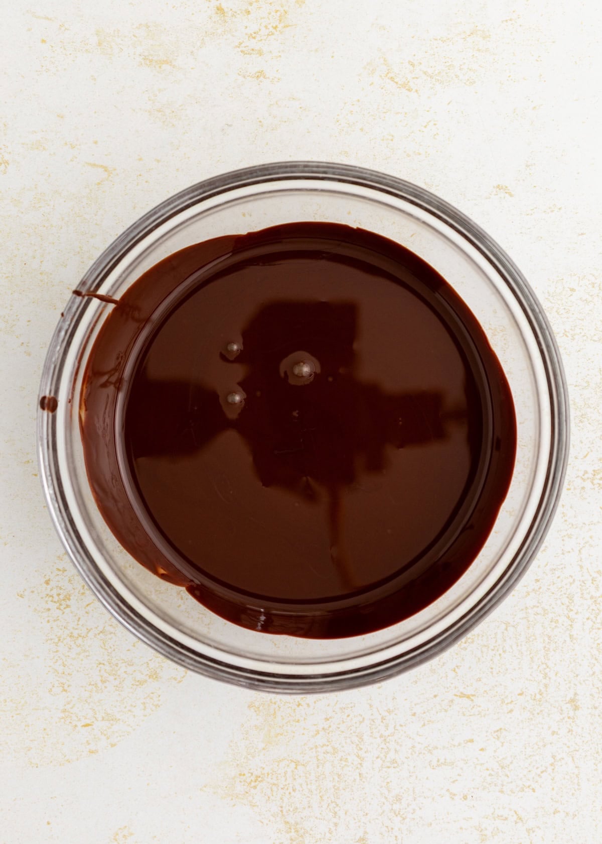 A glass bowl of smooth, melted dark chocolate for making Peanut Butter Oat Cups.