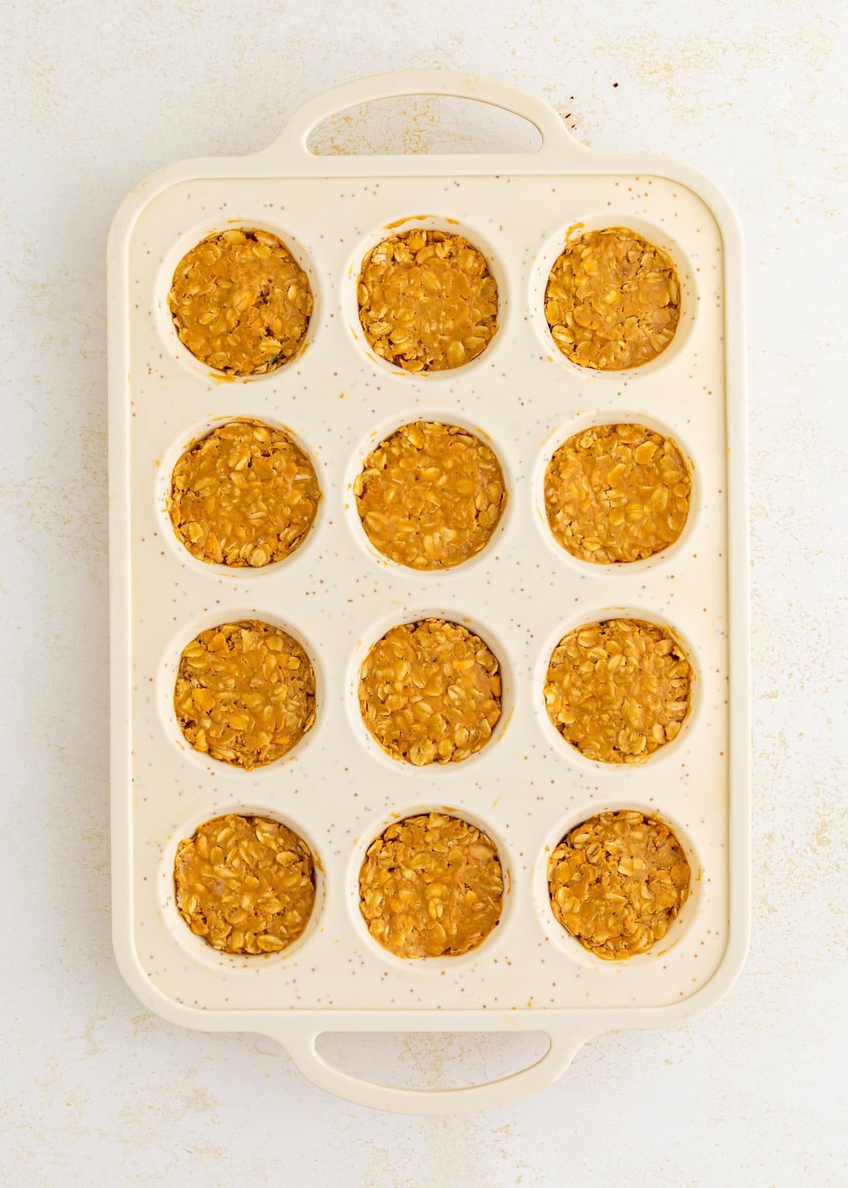 A muffin tin with twelve wells filled with Peanut Butter Oat Cups mixture.