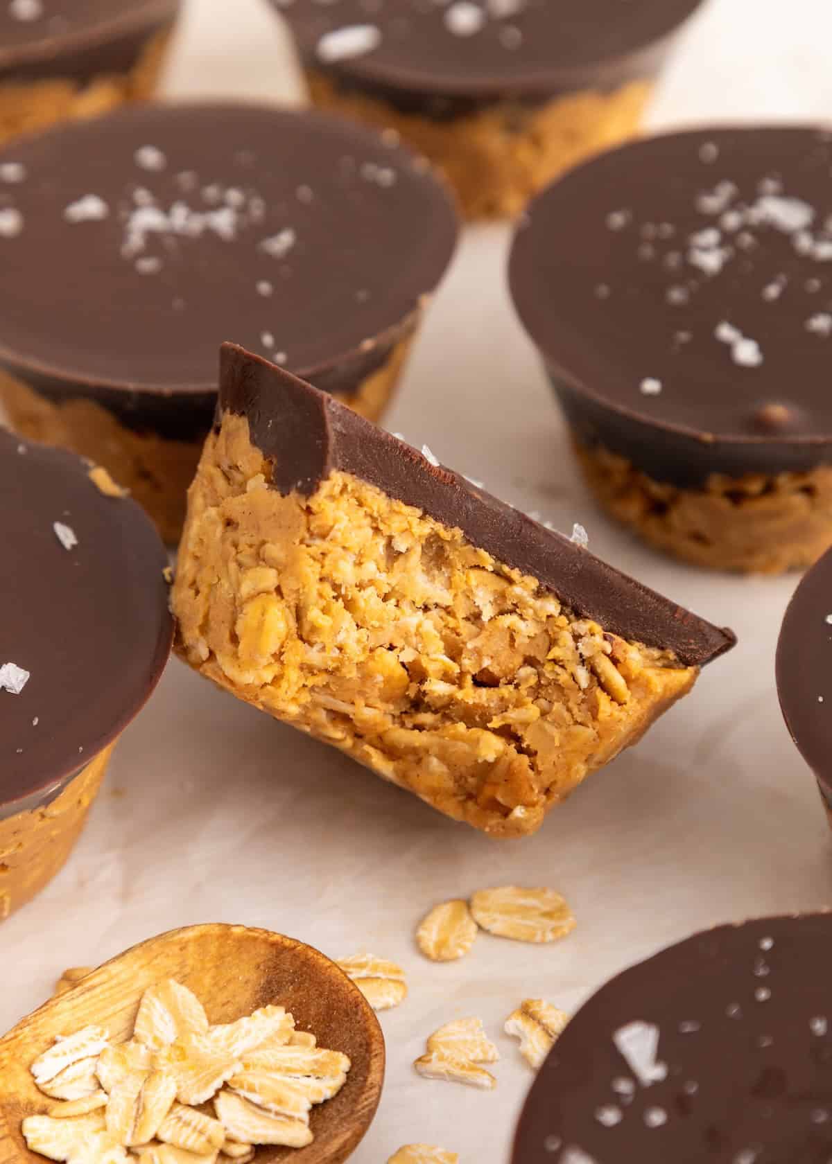 A Peanut Butter Oat Cups treat with chocolate topping, surrounded by more cups and oats.