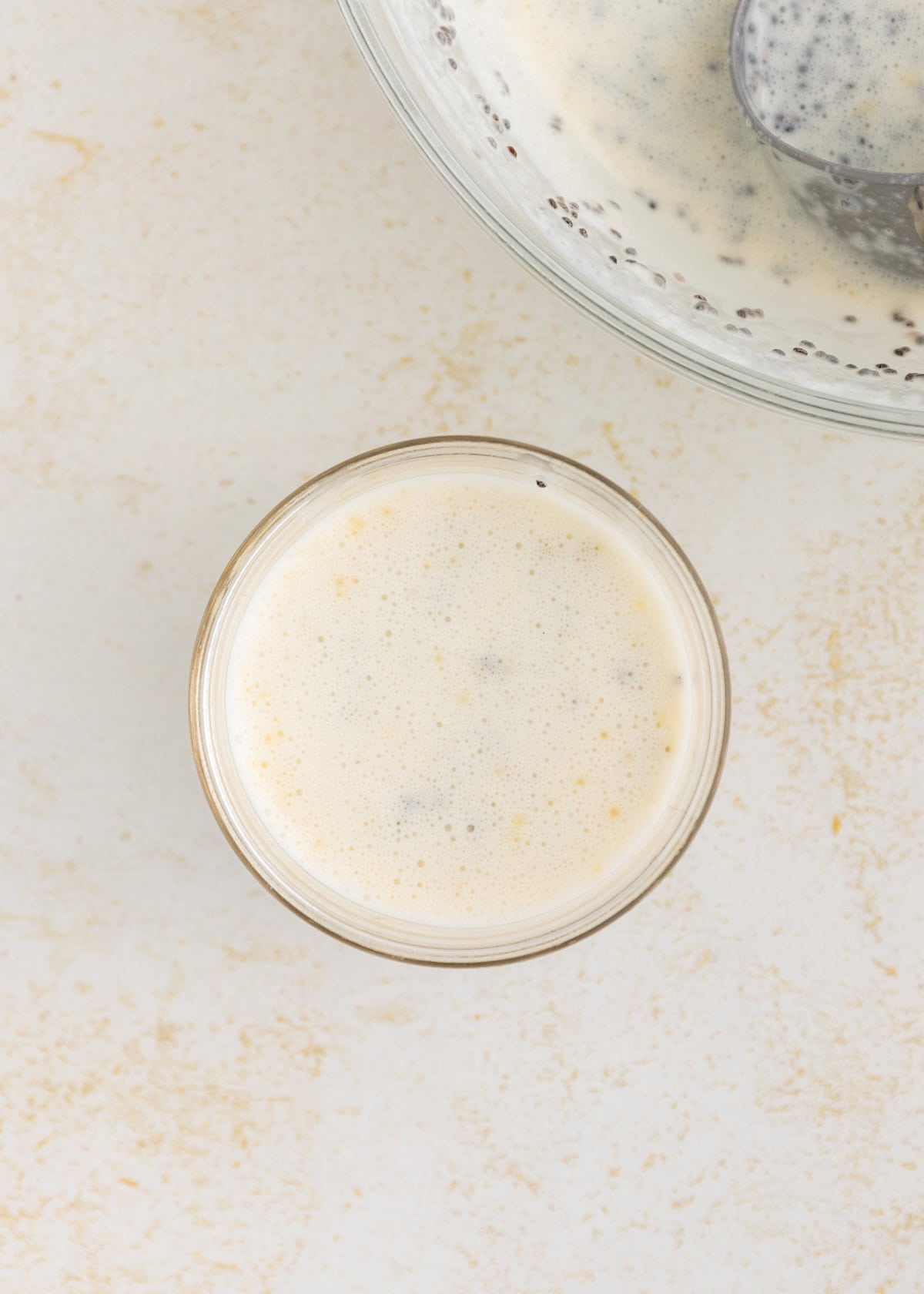 A glass of creamy Protein Chia Pudding next to a bowl with the same mixture on a light surface.
