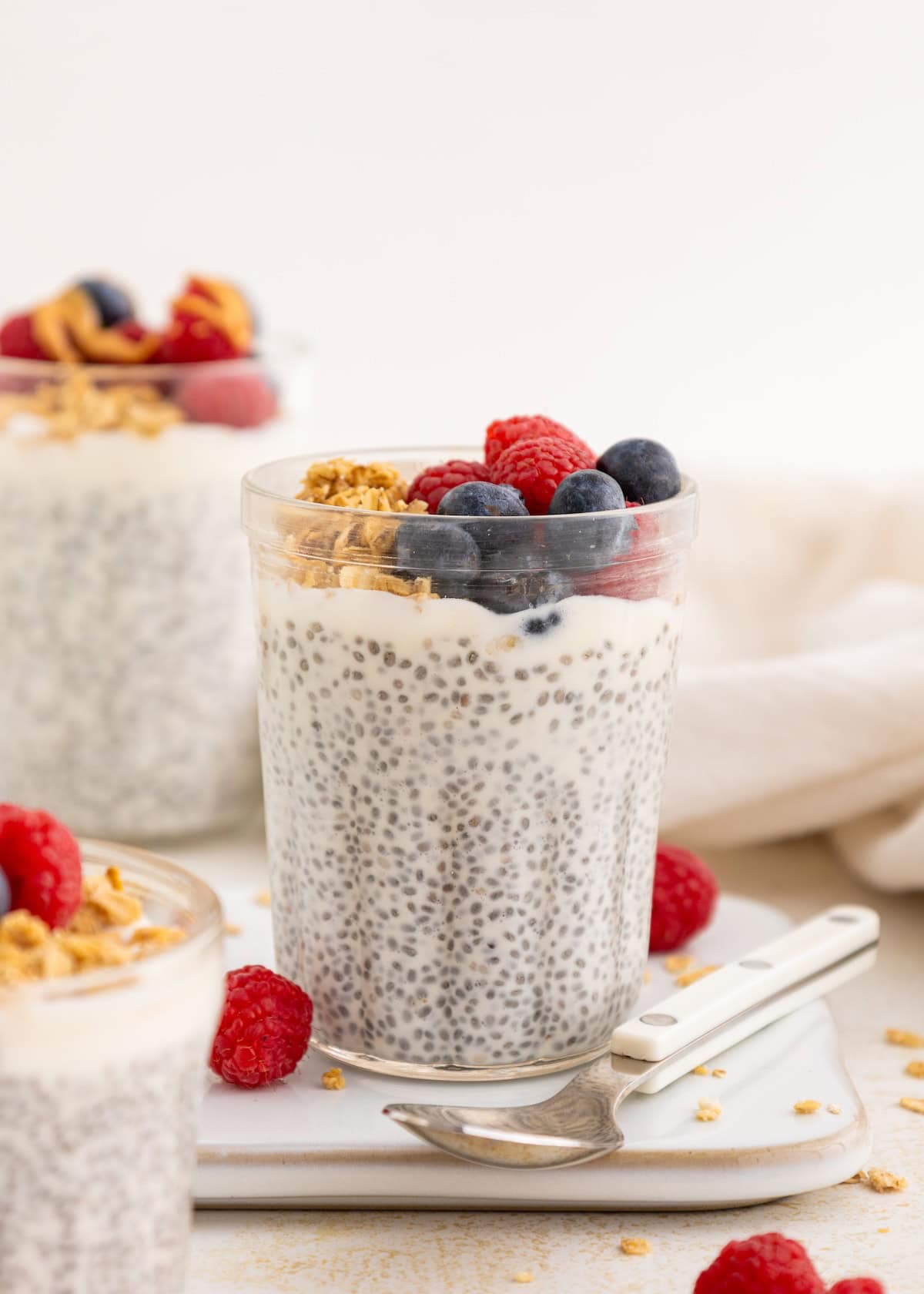 A glass of Protein Chia Pudding topped with berries and granola, with a spoon nearby.