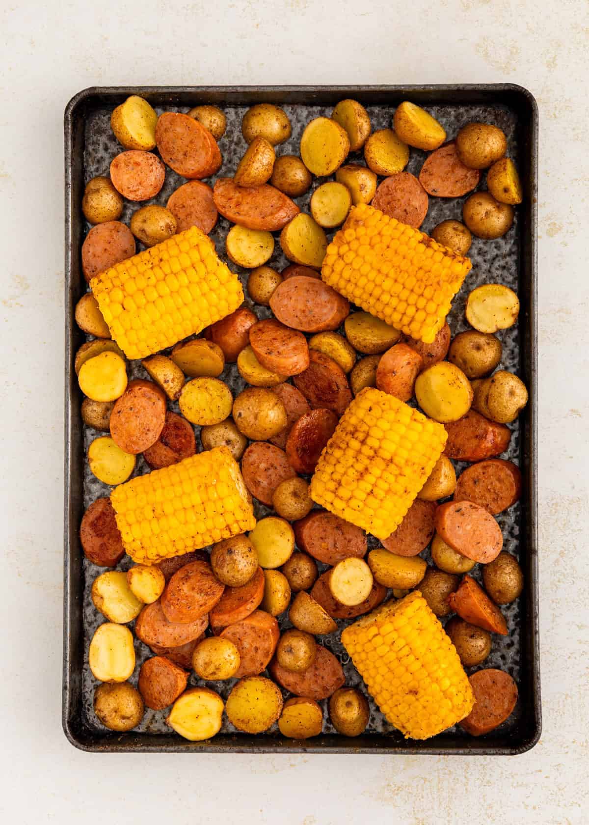 Corn and sliced potatoes on a baking sheet, ready to be roasted.