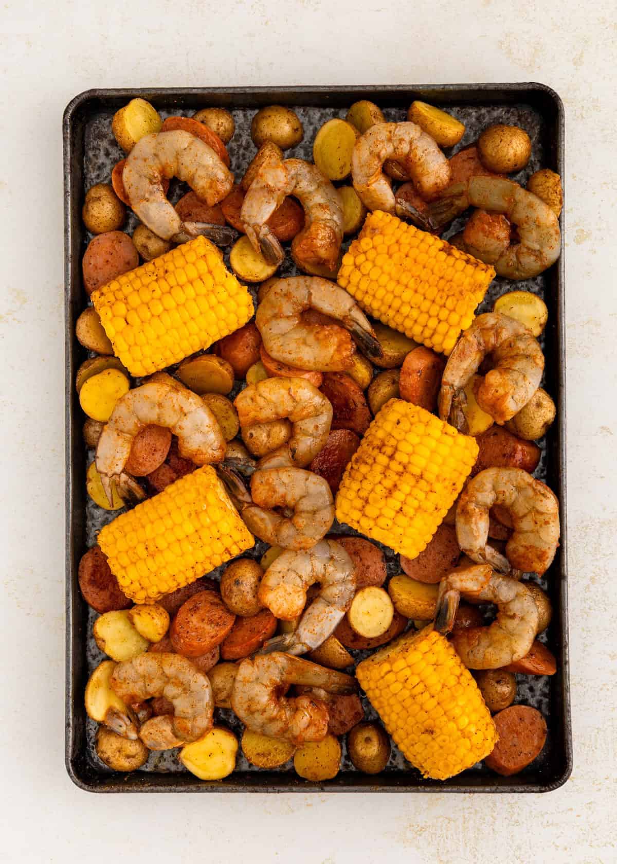 Sheet pan with shrimp, corn on the cob, sausage slices, and roasted potatoes.