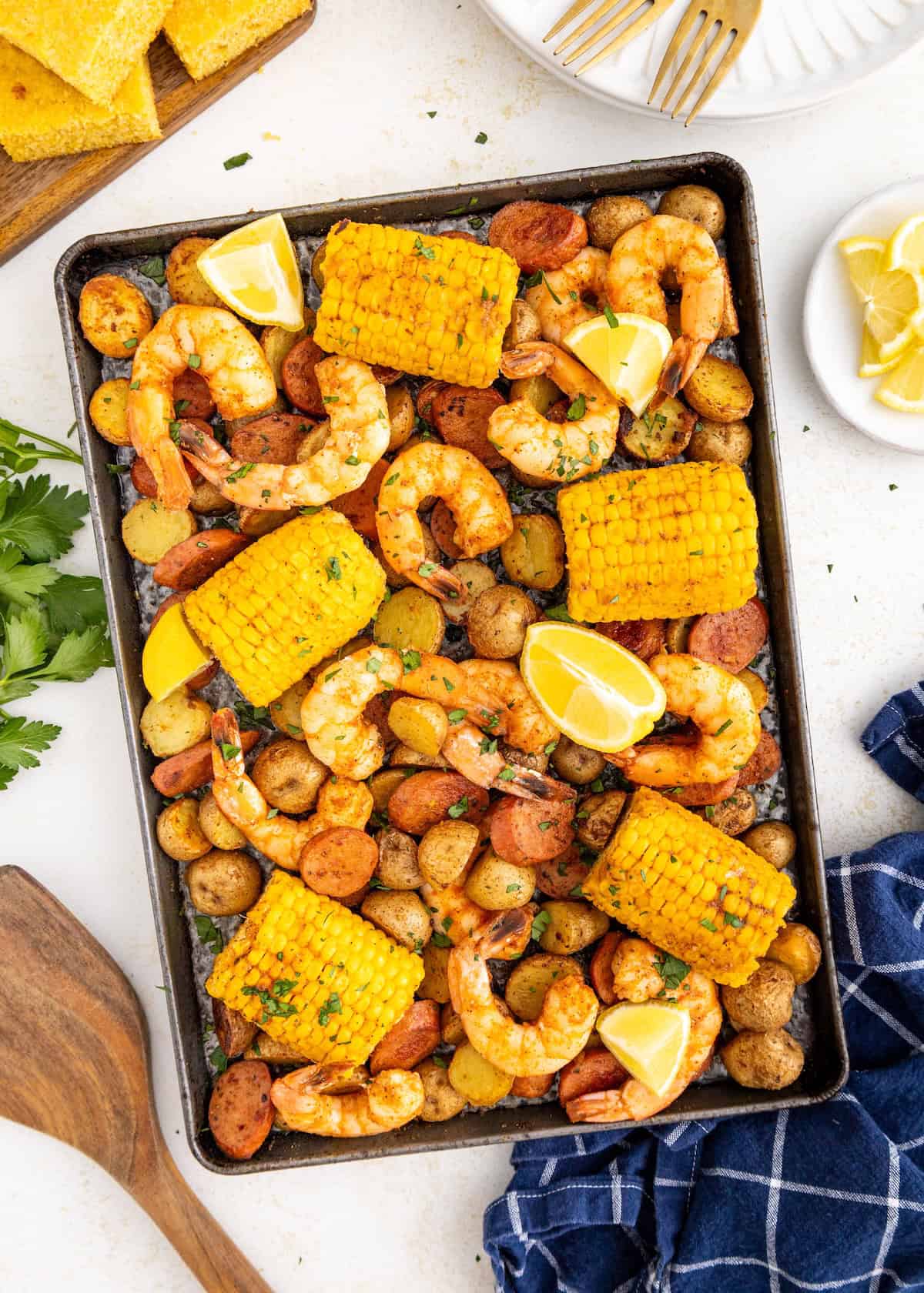 Sheet pan with shrimp, sausage, corn on the cob, potatoes, and lemon wedges.
