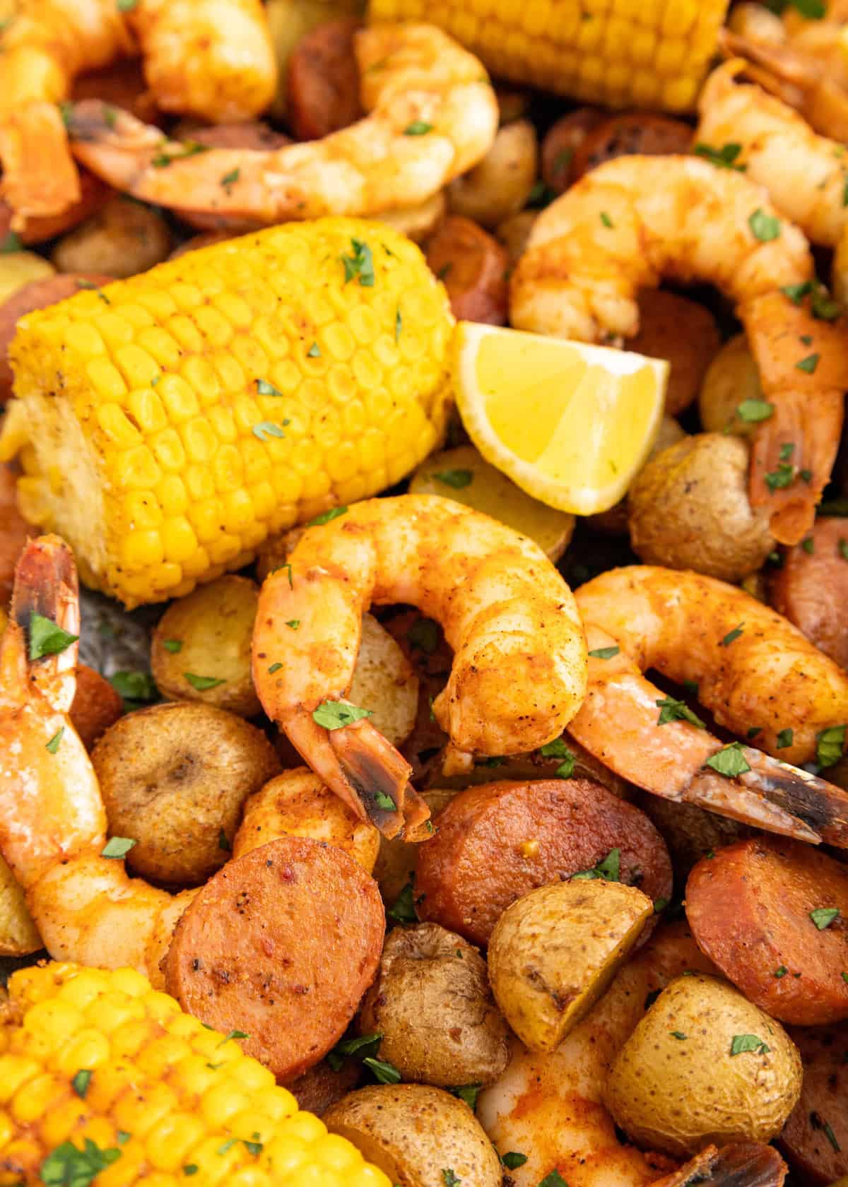 Shrimp, corn on the cob, sausage, potatoes, and lemon wedges, garnished with herbs.