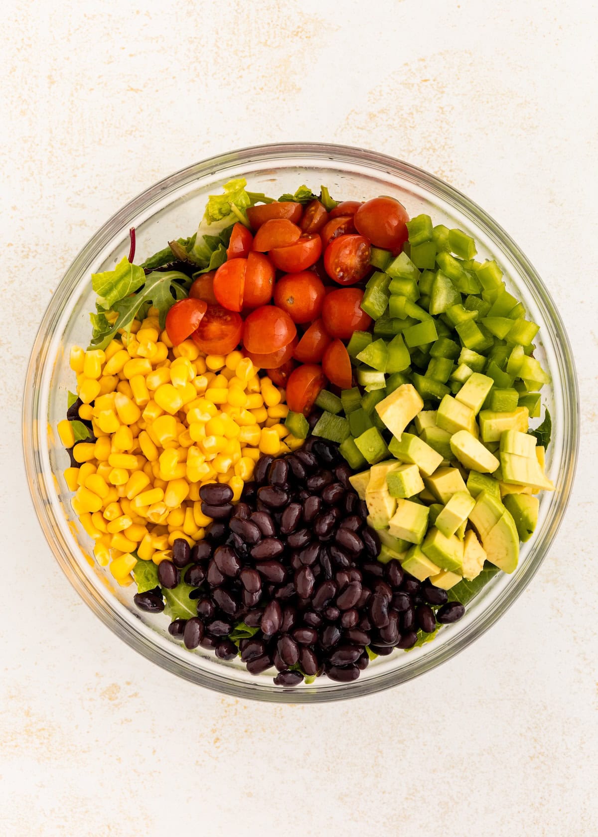 A bowl with lettuce, tomatoes, green peppers, avocado, black beans, and corn.