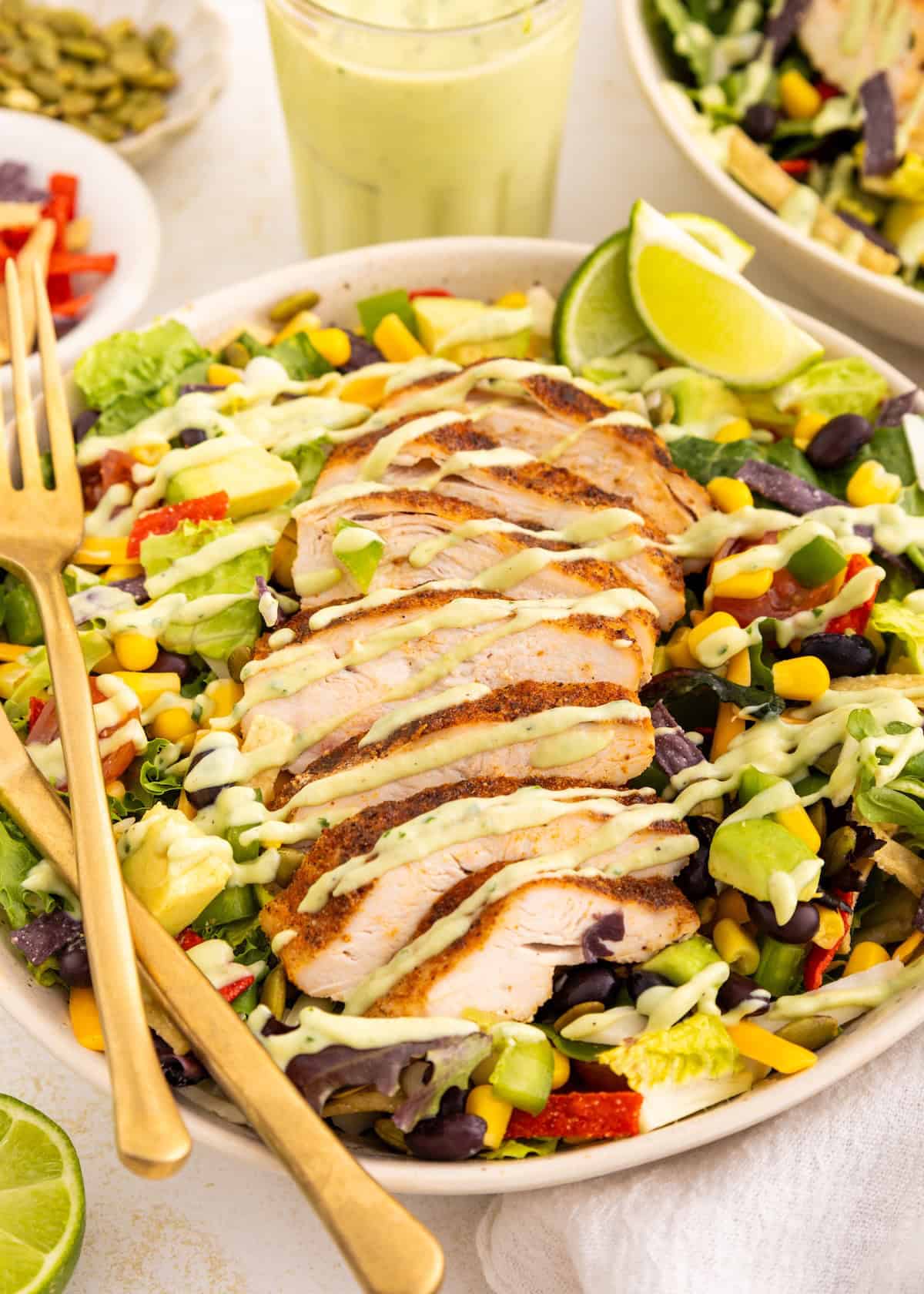 Sliced grilled chicken on a colorful salad with avocado, corn, and creamy dressing.