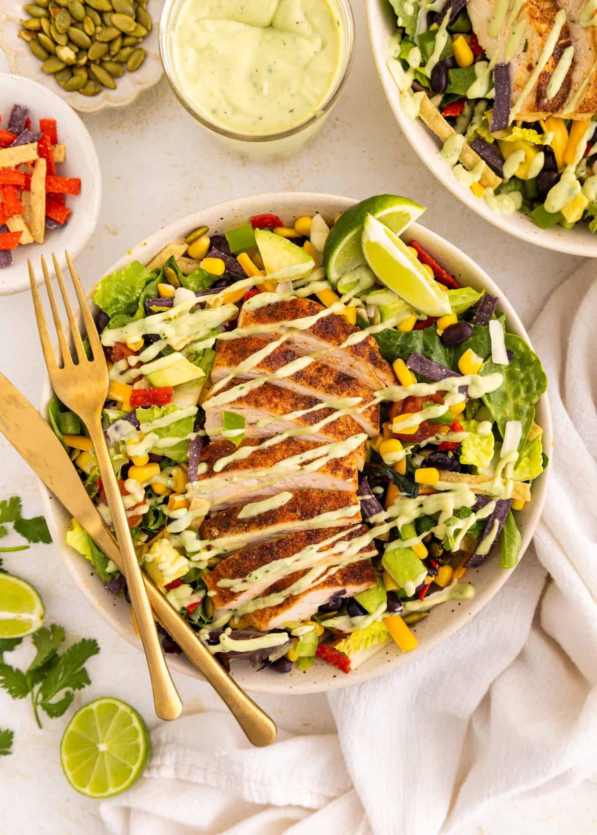 Southwest salad with grilled chicken, avocado, and dressing, garnished with lime wedges.