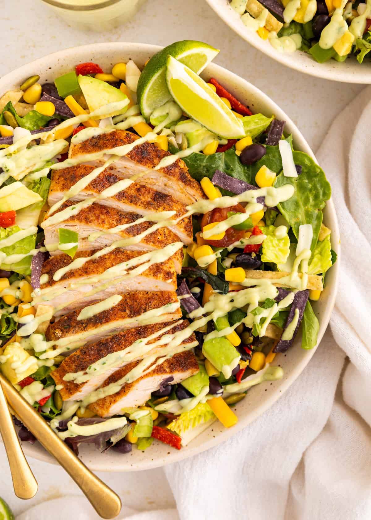 A salad bowl with grilled chicken, avocado, corn, tortilla strips, and creamy dressing.