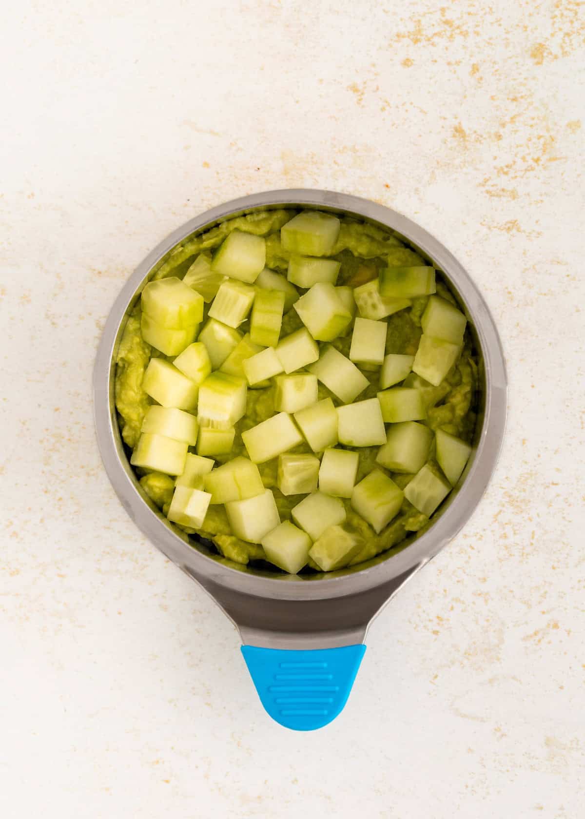 A bowl of mashed avocado topped with diced cucumber, perfect for sushi stacks.