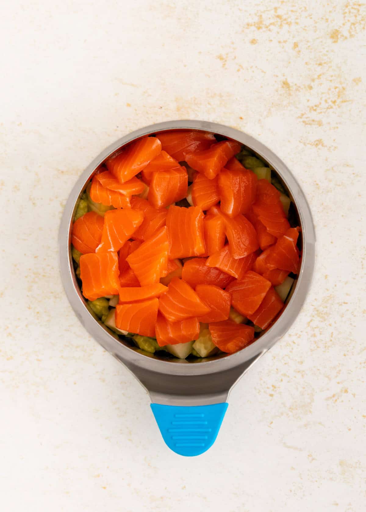 A bowl of diced raw salmon over veggies, served with a scoop-perfect for sushi stacks lovers.