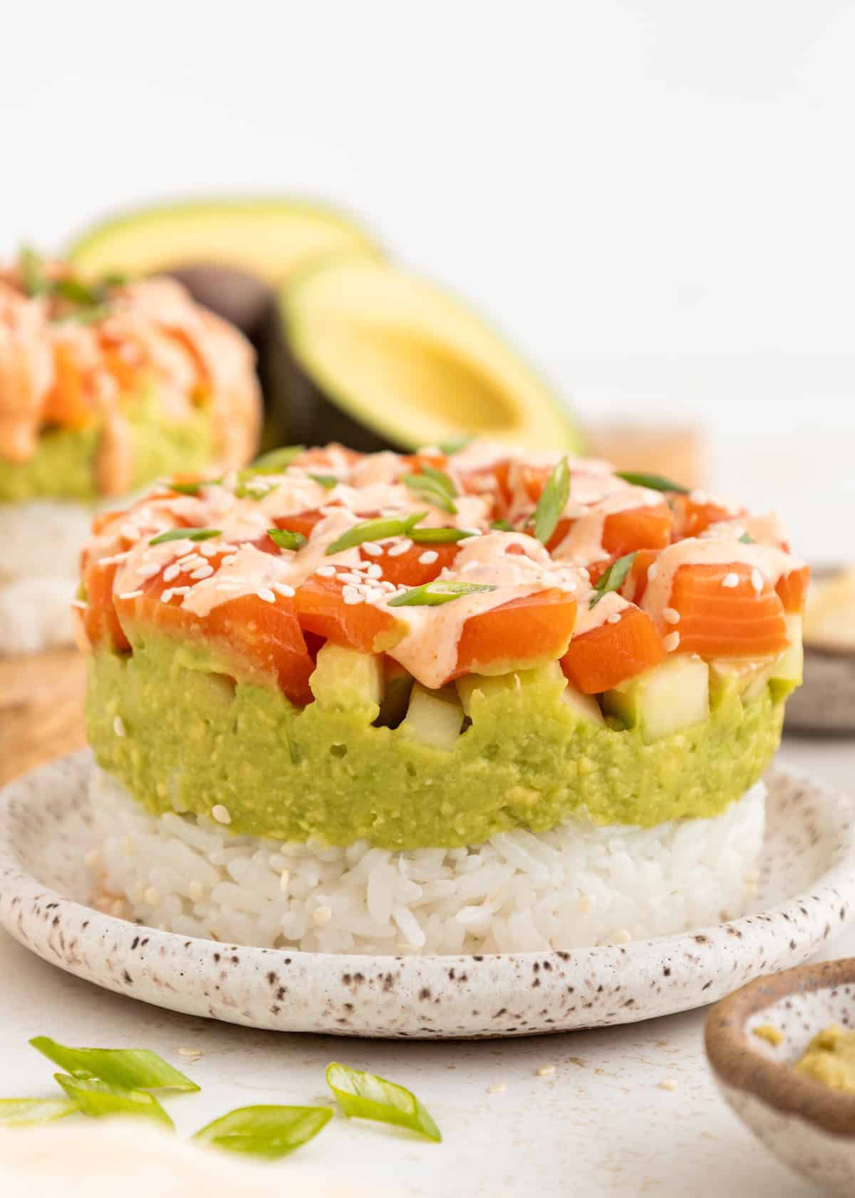 A sushi stack with rice, avocado, diced fish, sauce, and sesame seeds—classic sushi stacks.