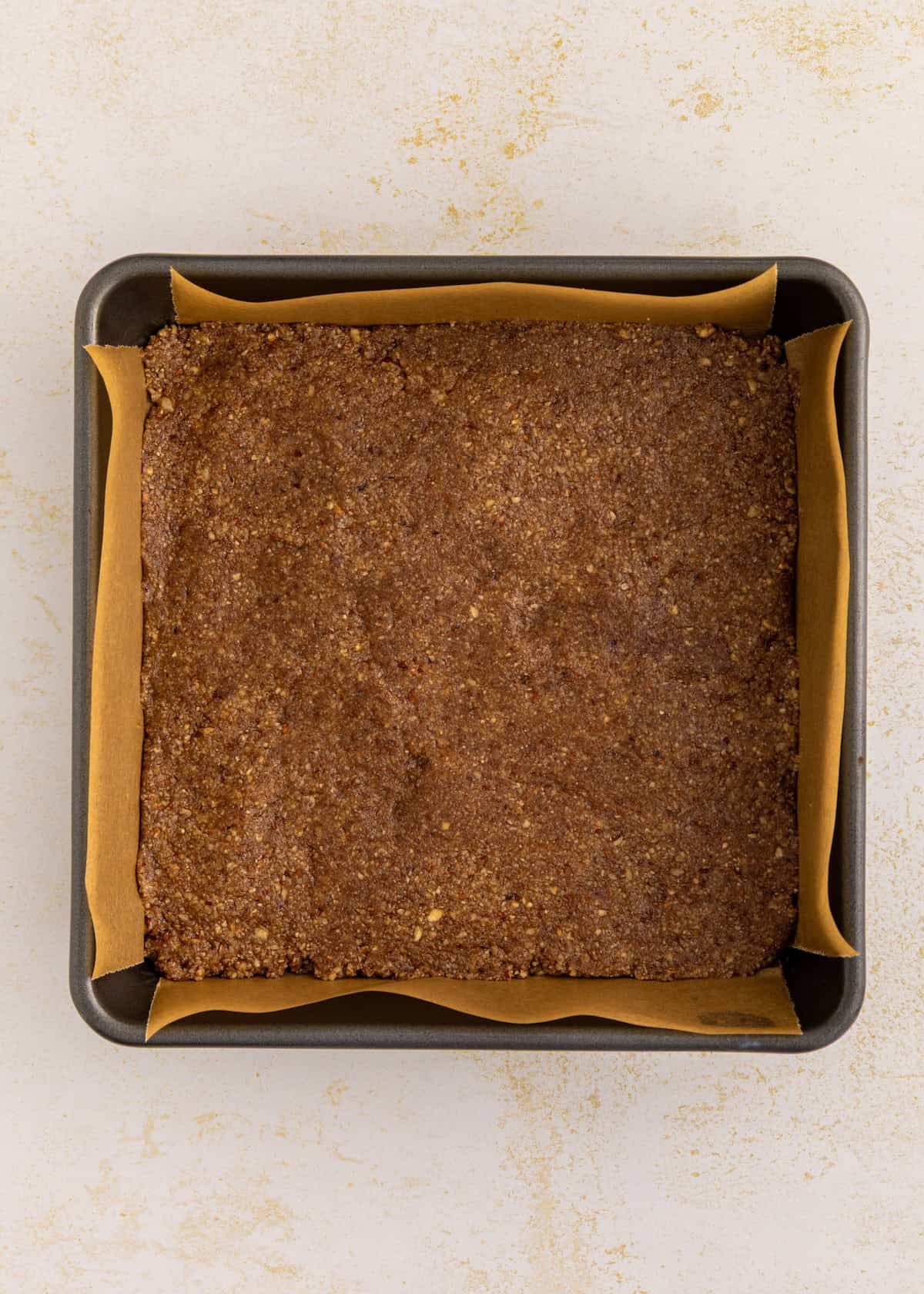A square pan lined with parchment, ready for sweet potato pie bars and an unbaked brown crust.