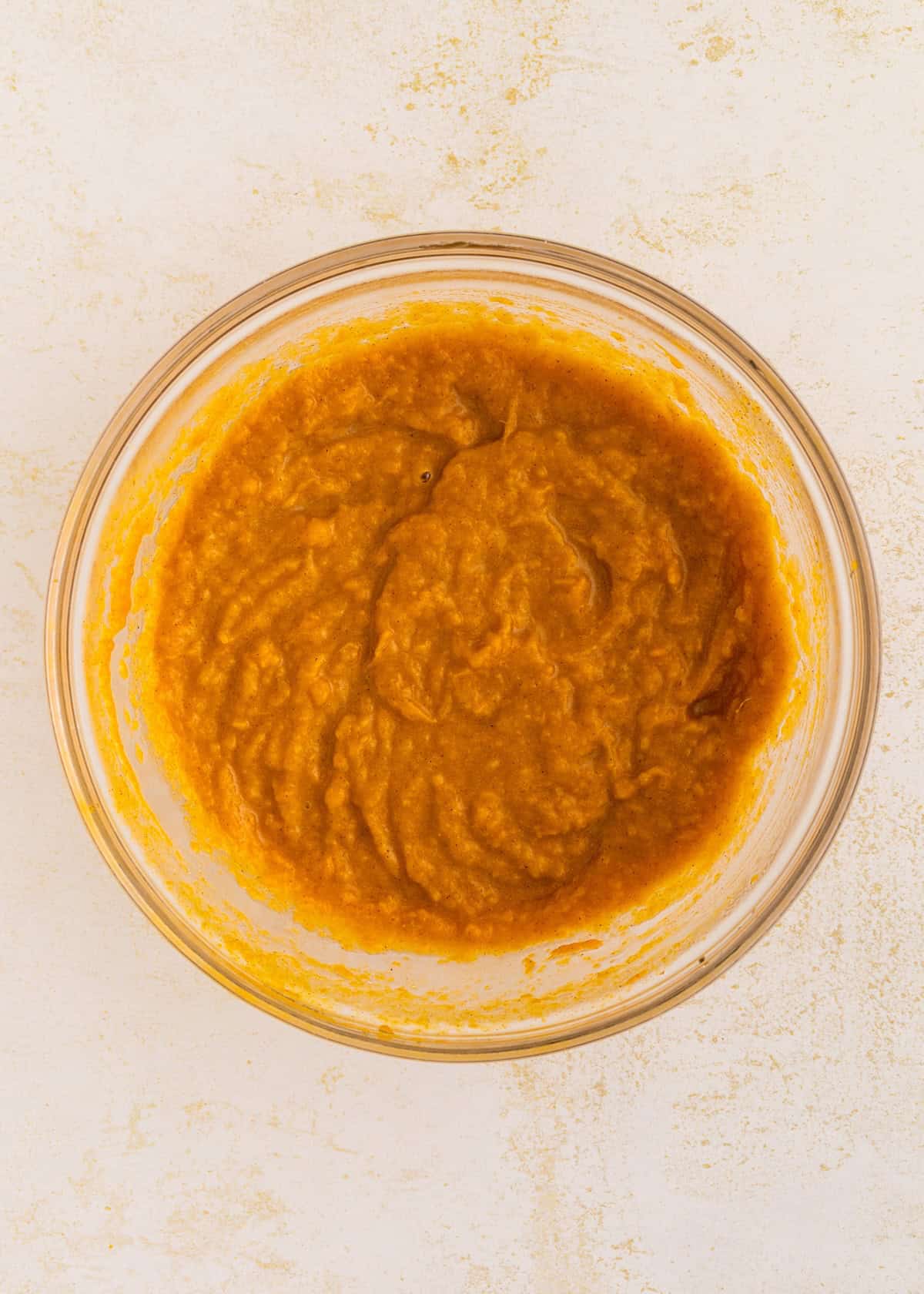 Clear glass bowl filled with smooth sweet potato pie bars batter on a light-colored surface.