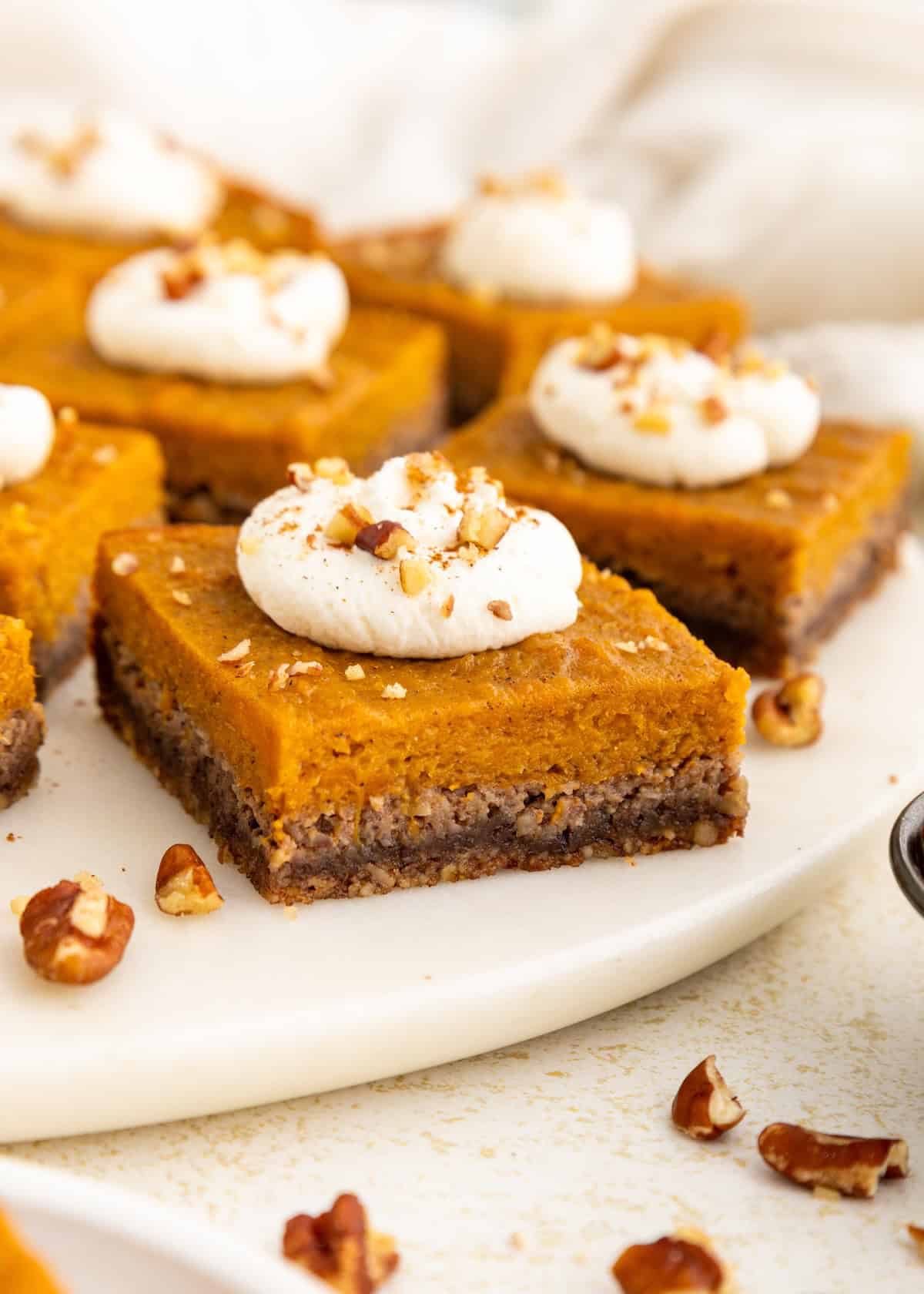 Sweet potato pie bars with whipped cream and chopped nuts on a white plate.