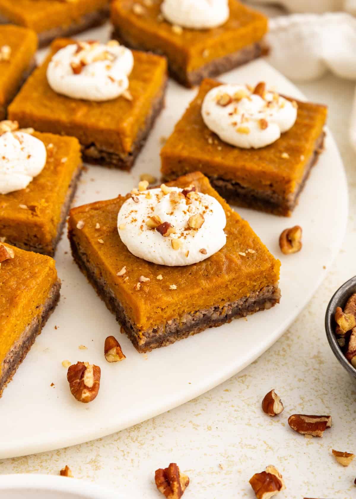 Sweet potato pie bars topped with whipped cream and pecans on a white platter.