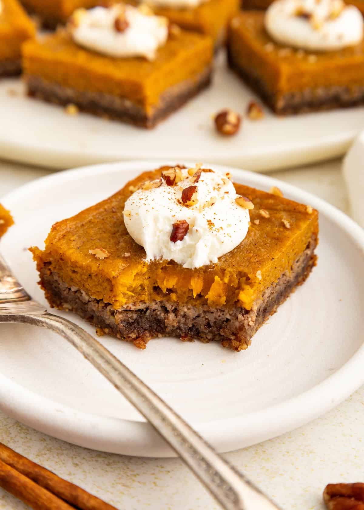 A sweet potato pie bars dessert with whipped cream and chopped nuts on a white plate, one bite taken.