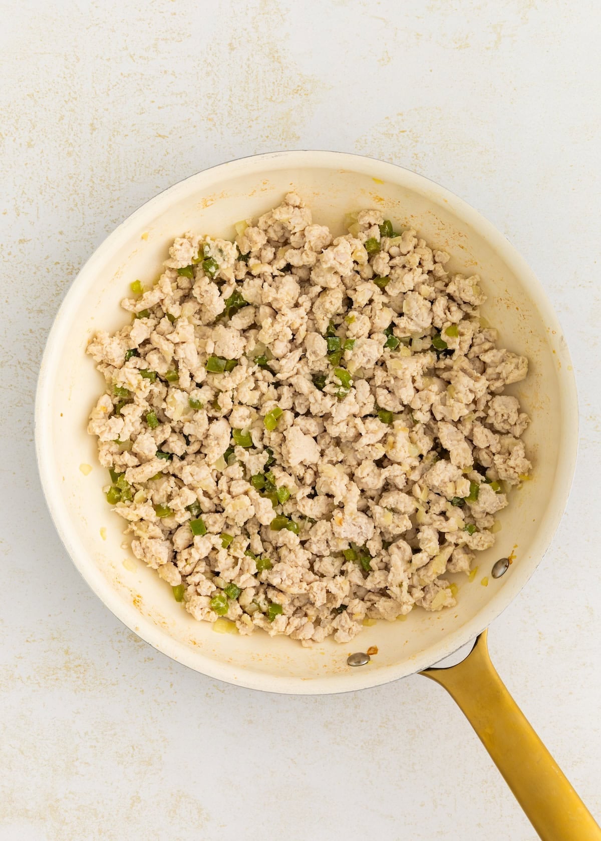 Turkey sloppy joes with chopped vegetables in a yellow-handled frying pan on a light surface.