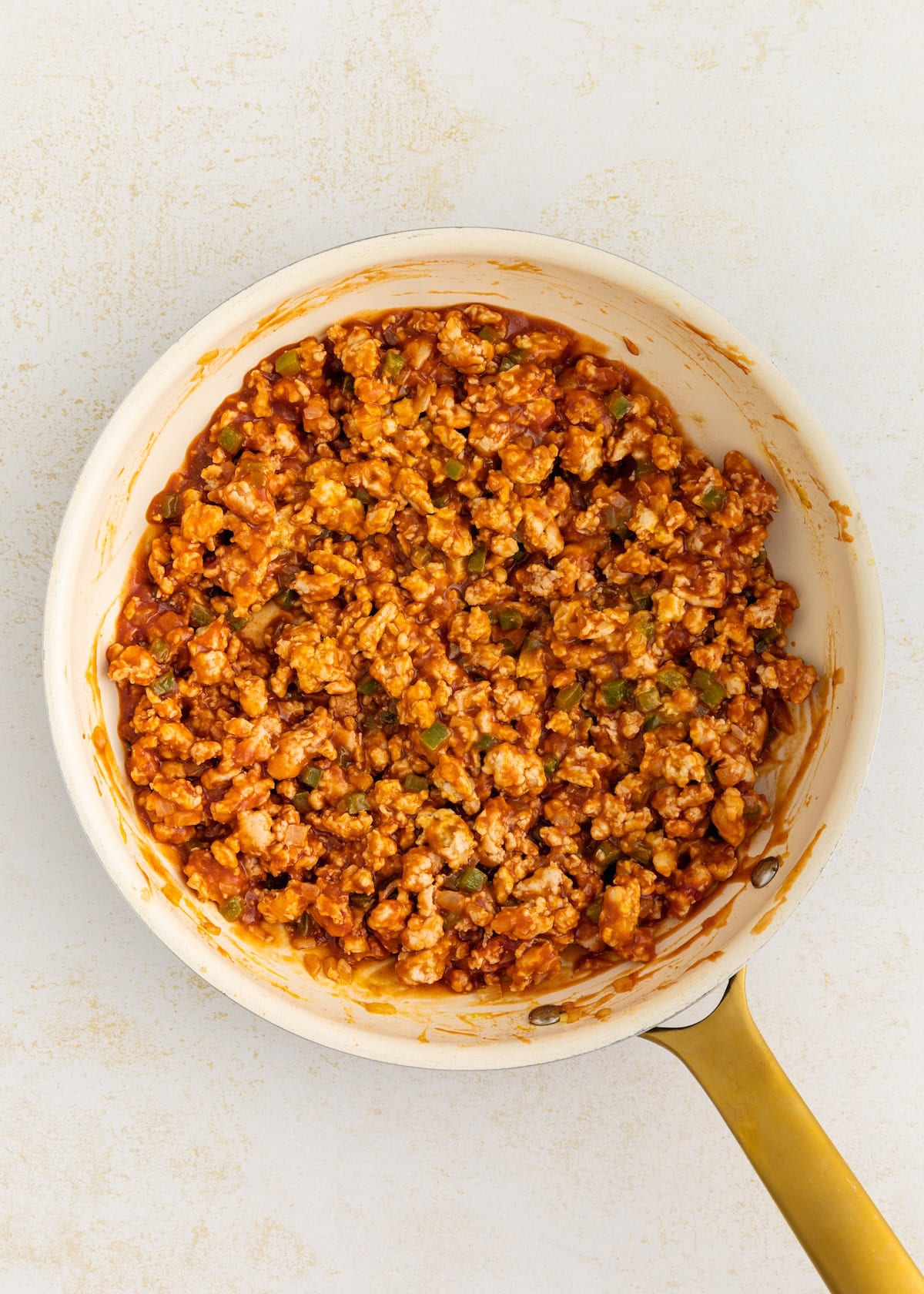 Turkey sloppy joes cooked with sauce and veggies in a white skillet with a gold handle.