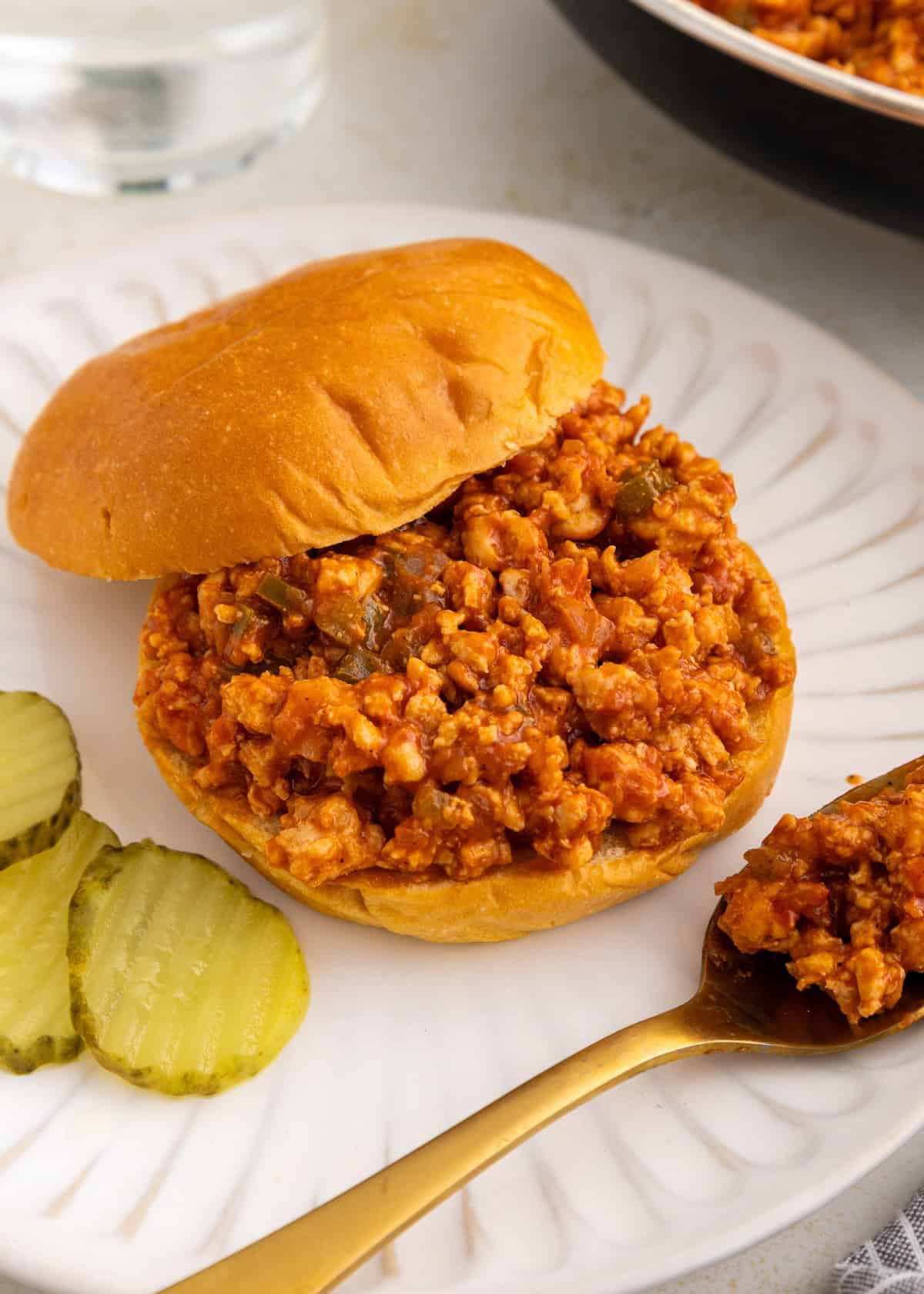 Turkey sloppy Joes sandwich on a plate with pickle slices and a spoonful of filling nearby.