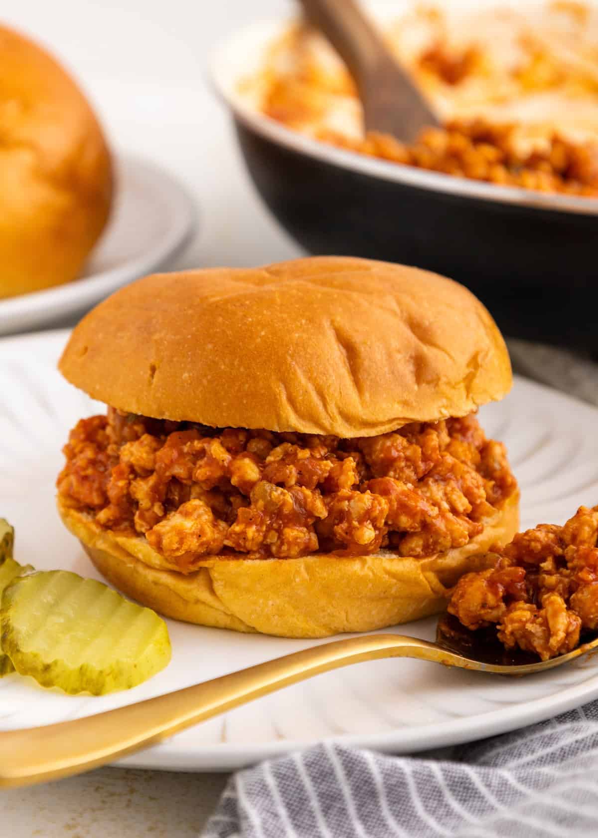 Turkey sloppy joes sandwich on a plate with pickles and a spoonful of filling nearby.