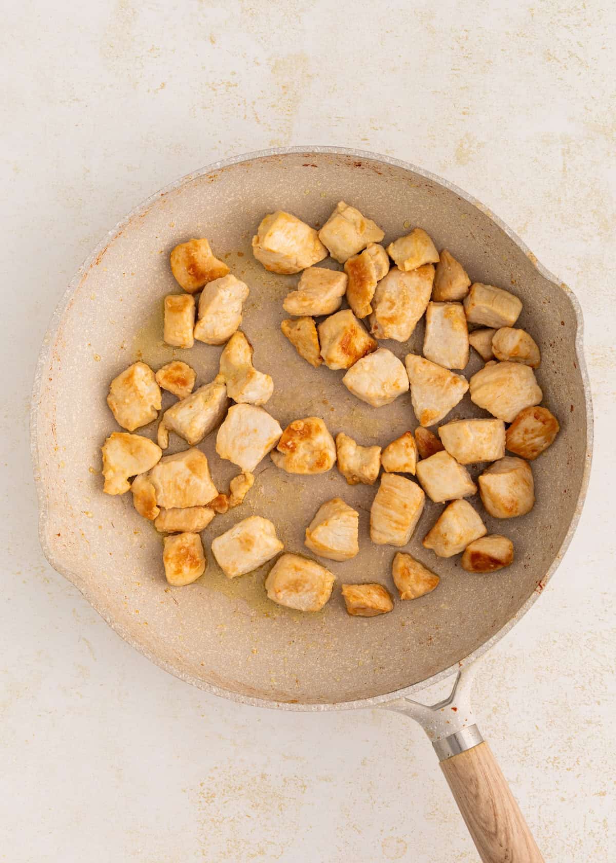 Thai Basil Chicken pieces cooked in a frying pan on a light-colored surface.