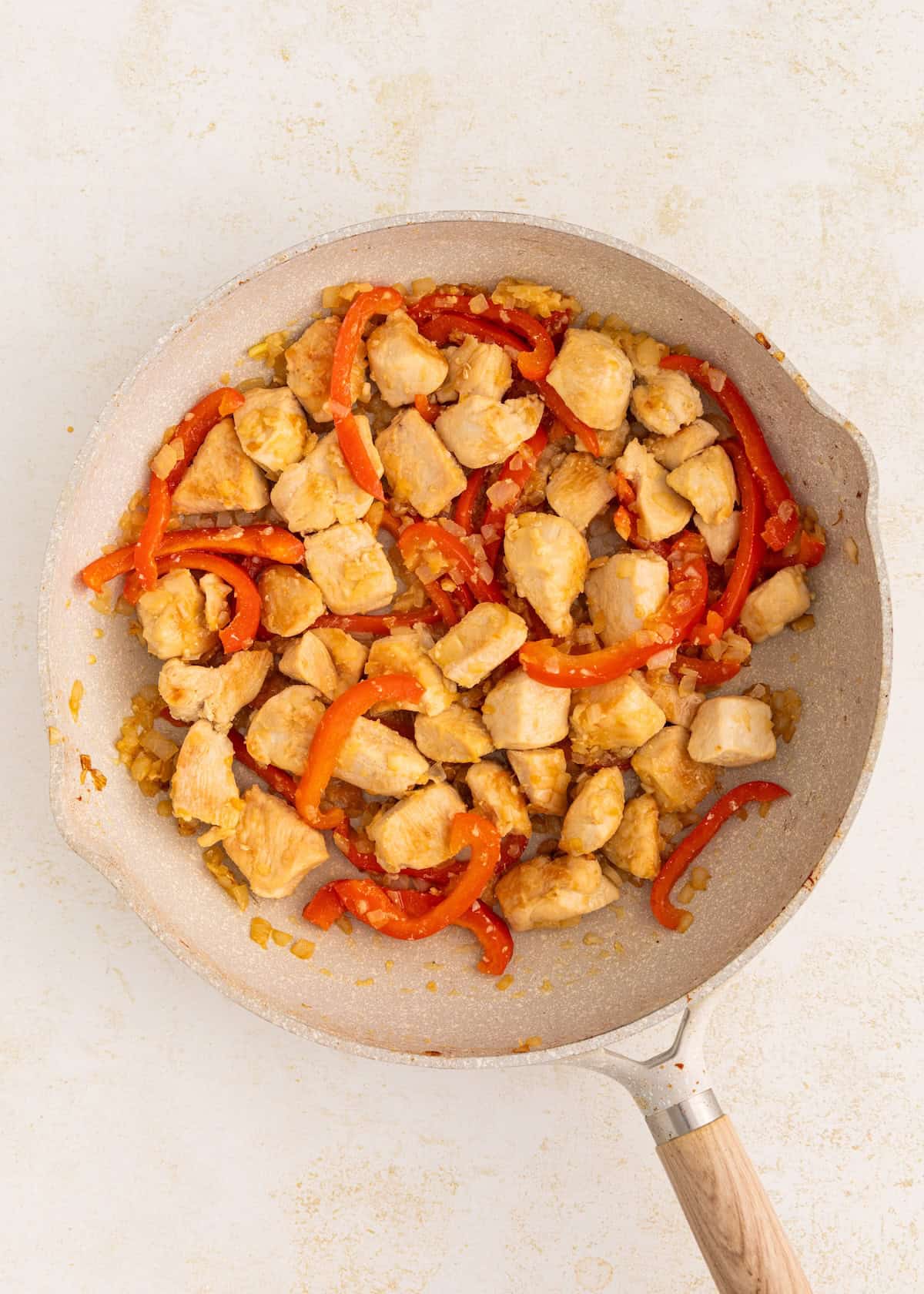 Thai Basil Chicken with red bell peppers cooked in a skillet on a light background.