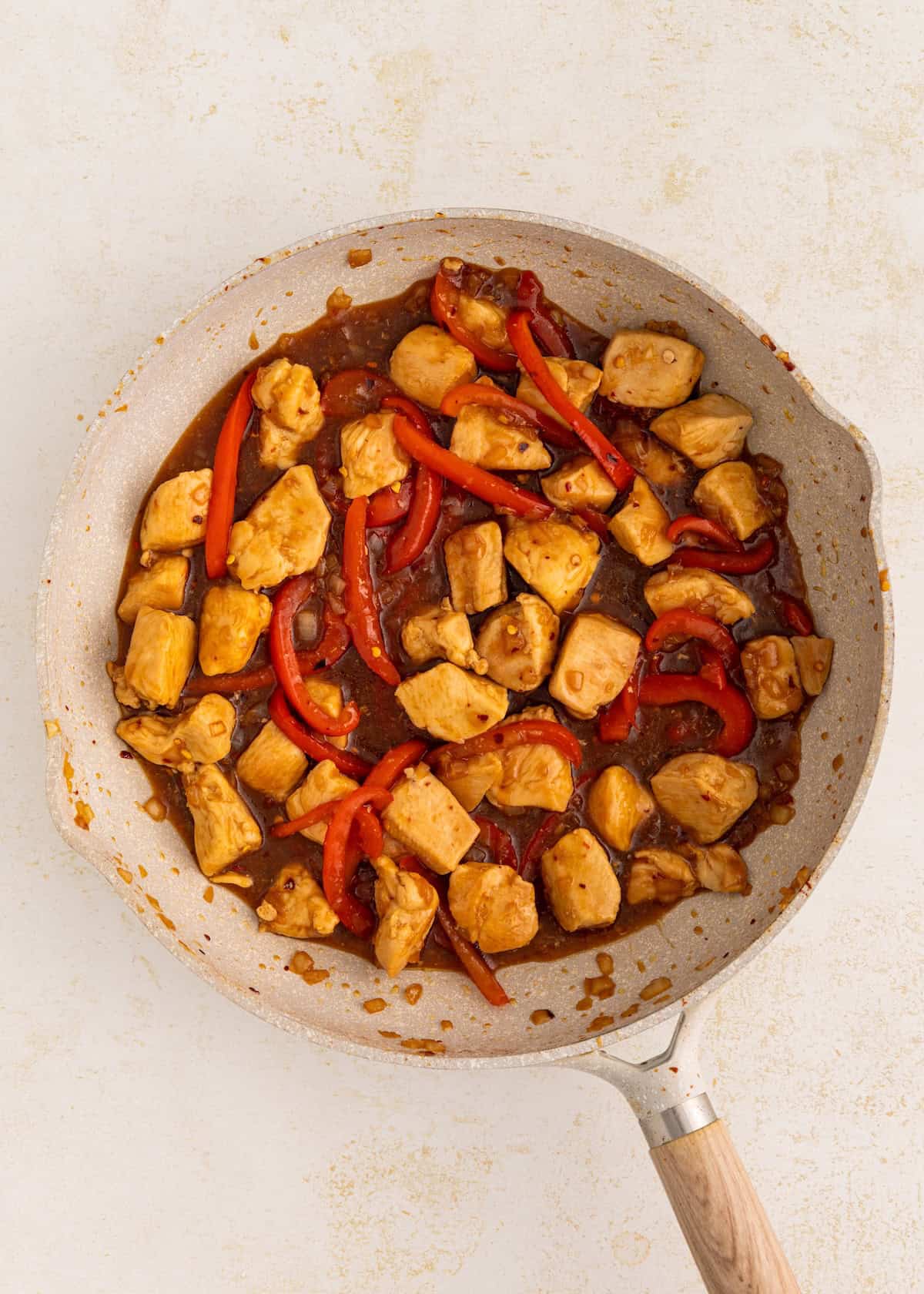 Thai Basil Chicken and red bell peppers sizzling in a skillet with savory sauce.