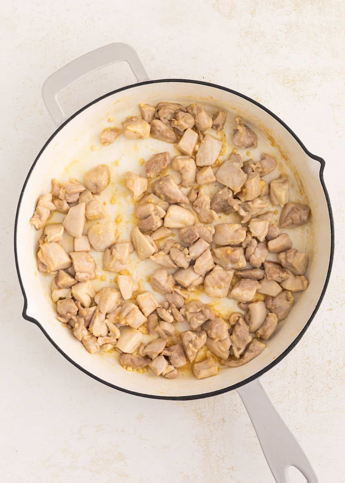 Cooked pieces of chicken in a white skillet on a light-colored surface.