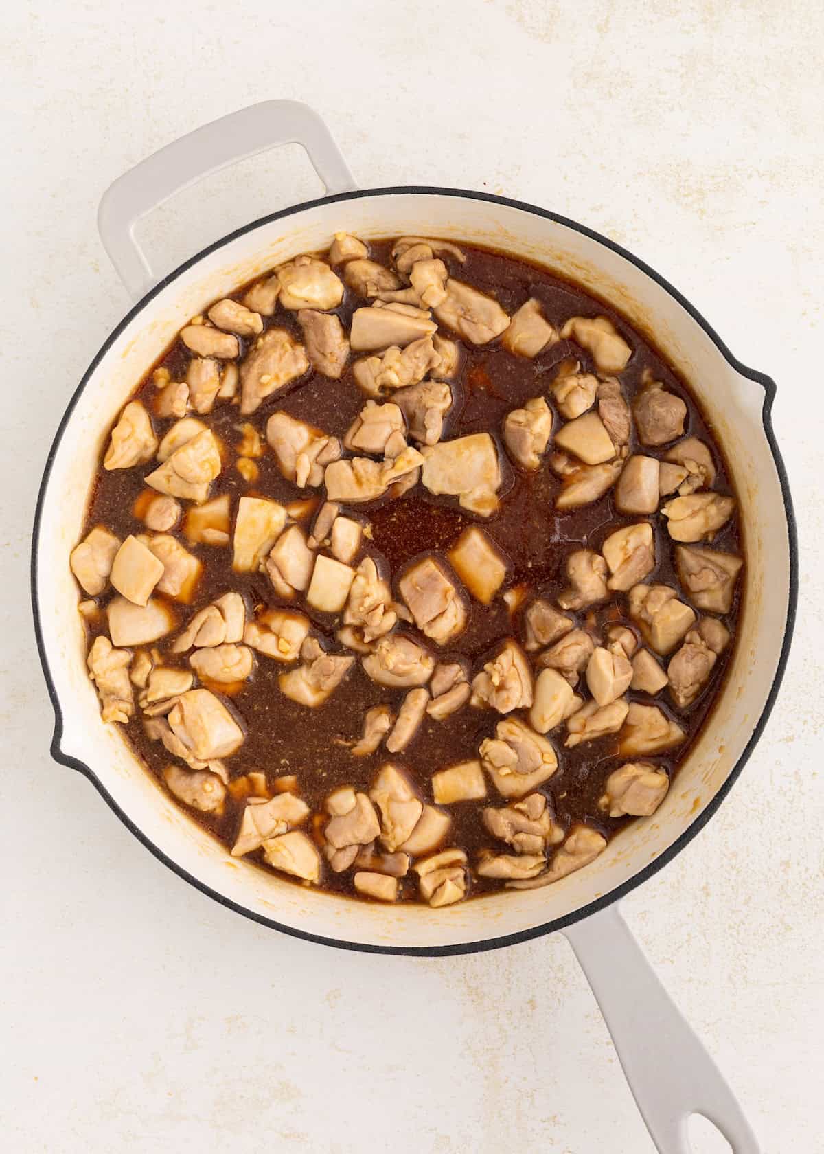 Chopped chicken pieces cooking in a round white pot with a dark brown sauce.