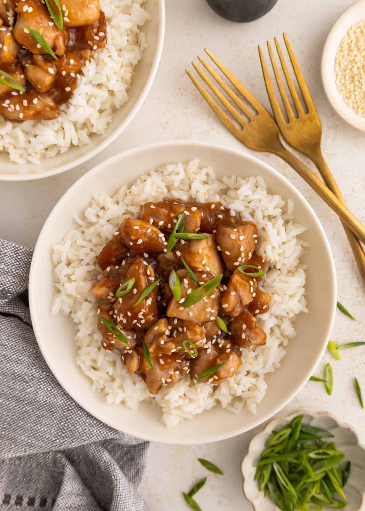 Bowl of white rice topped with teriyaki chicken, sesame seeds, and sliced green onions.