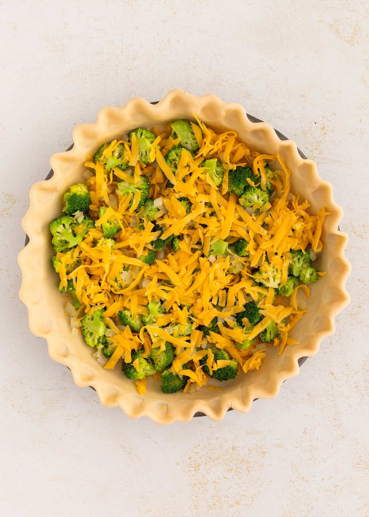 Unbaked pie crust filled with chopped broccoli and shredded cheddar cheese.