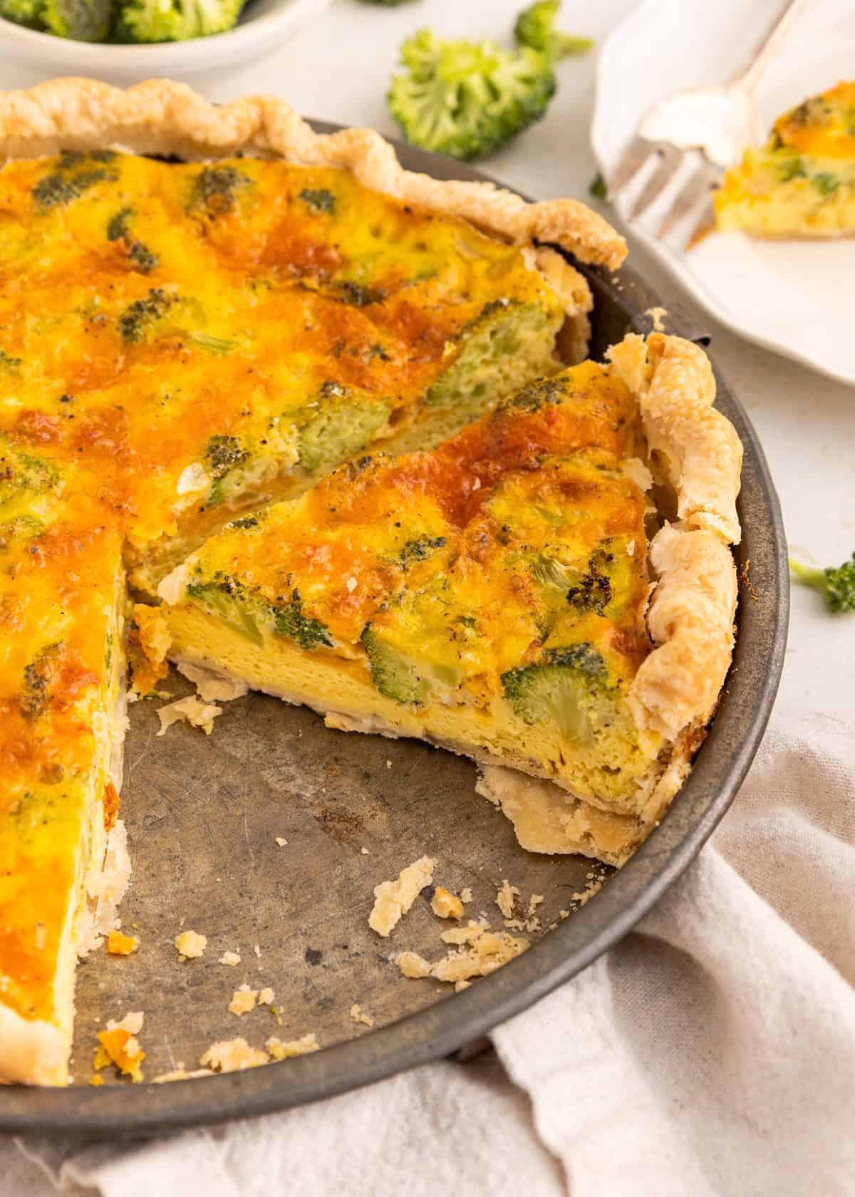 Broccoli and cheese quiche with a slice missing in a metal pie pan.