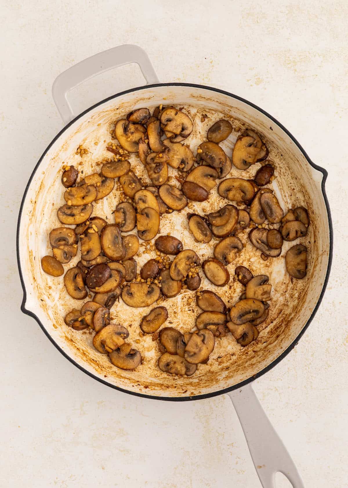 Sautéed mushrooms in a white skillet on a light-colored surface.
