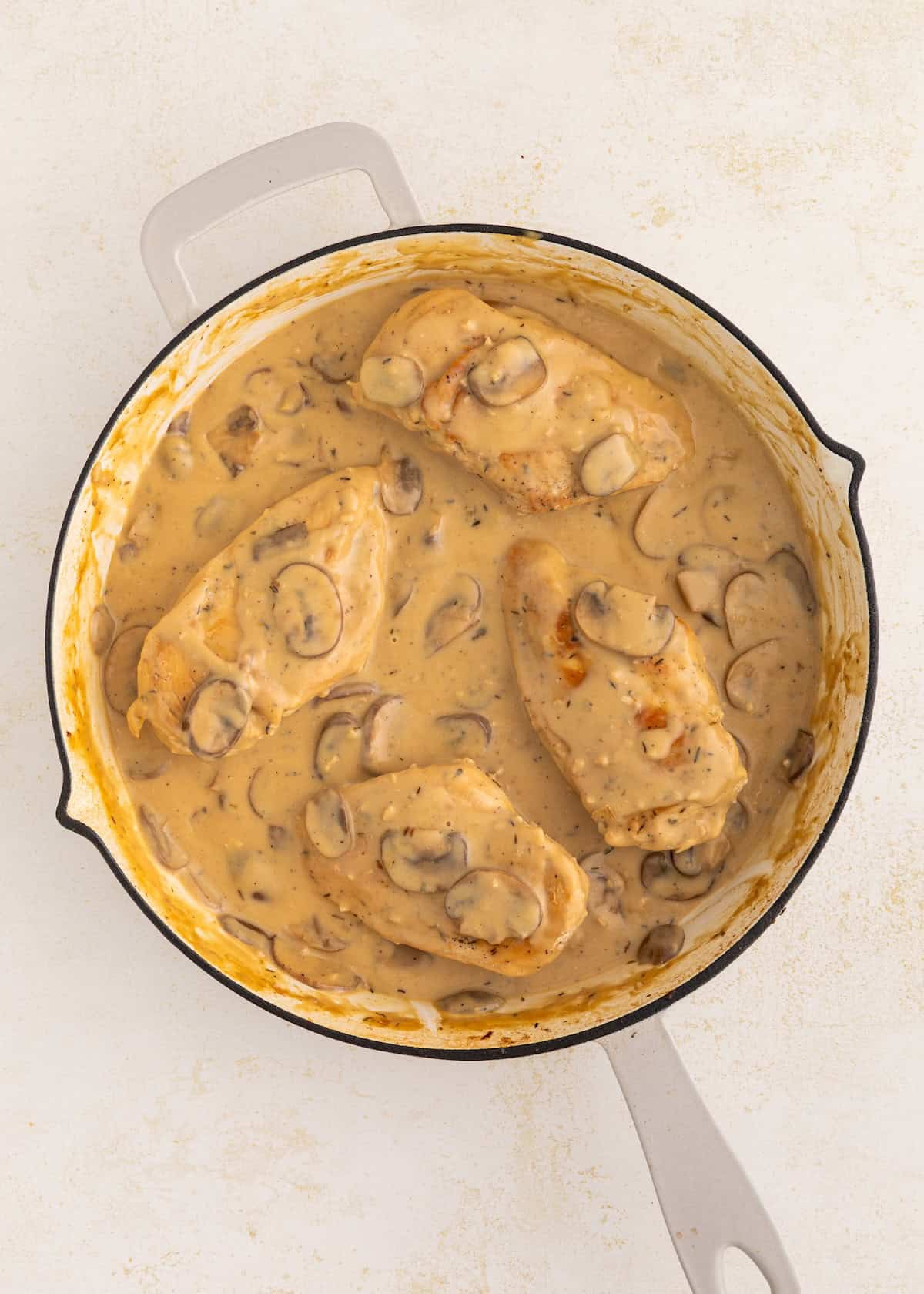 Chicken breasts in creamy mushroom sauce in a round white skillet on a light background.