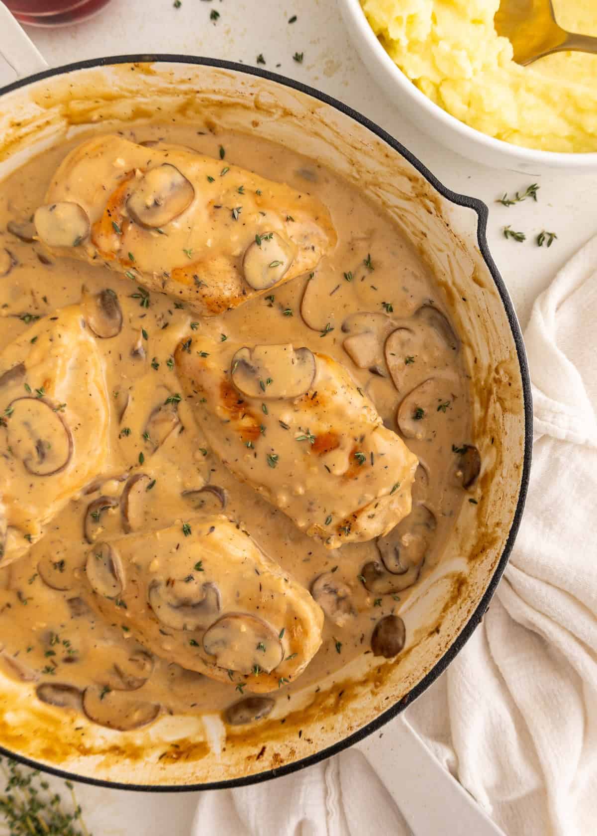 Chicken breasts in creamy mushroom sauce in a skillet, served with mashed potatoes nearby.